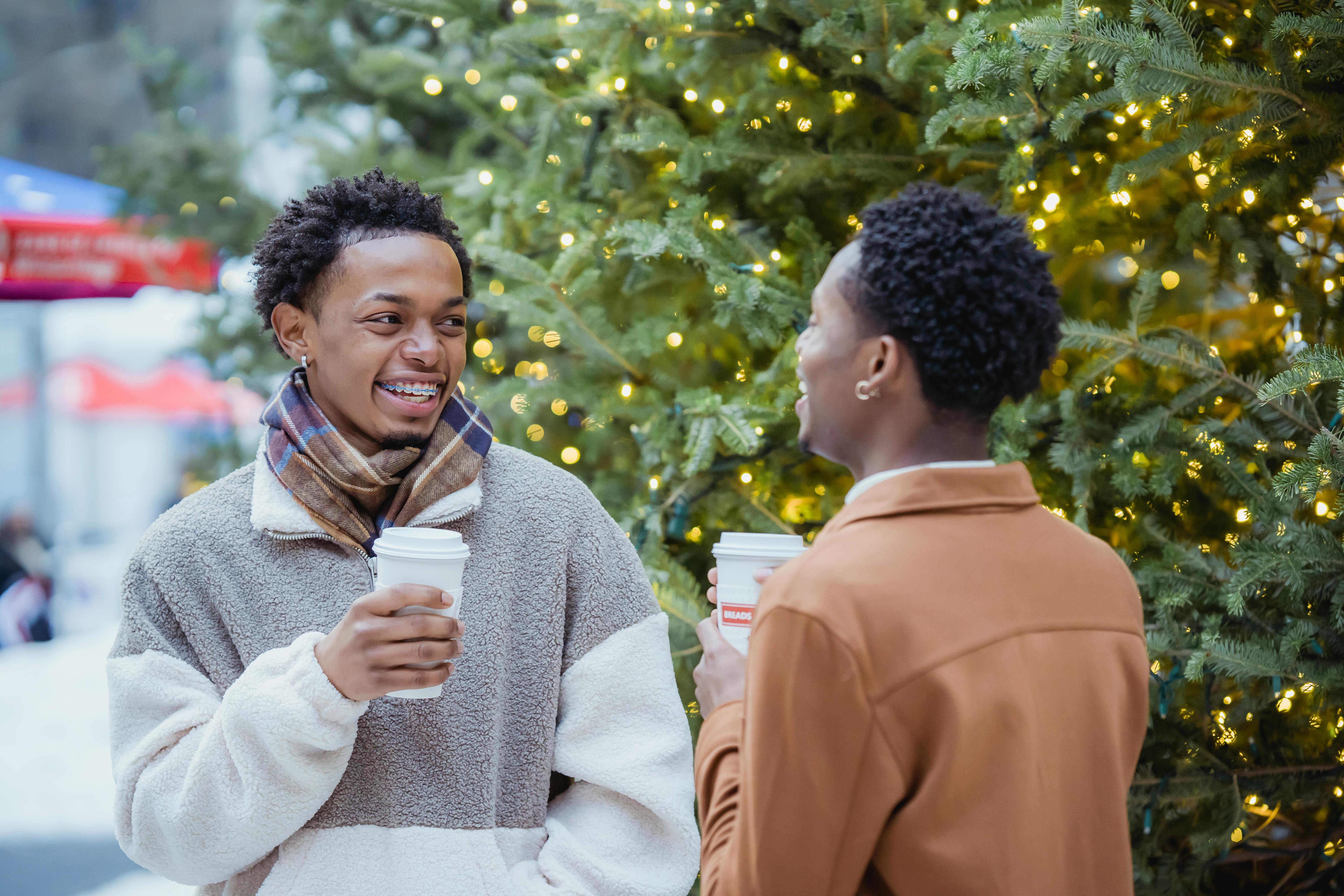 cheerful young black gays drinking coffee and laughing on street during xmas holidays