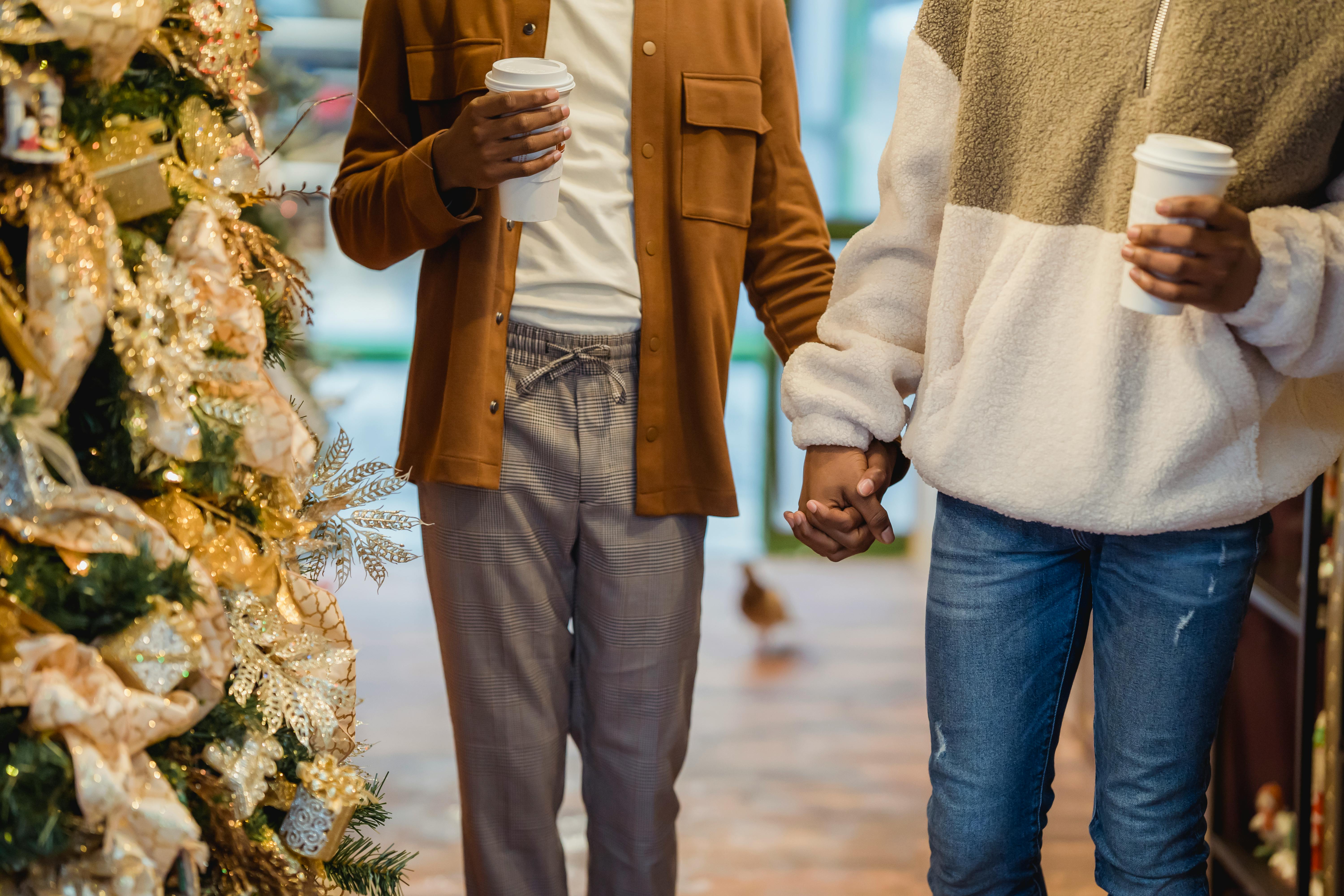 crop ethnic gay couple holding hands while walking in city during xmas holidays