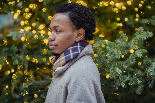 Young black guy standing near decorated Christmas tree in city