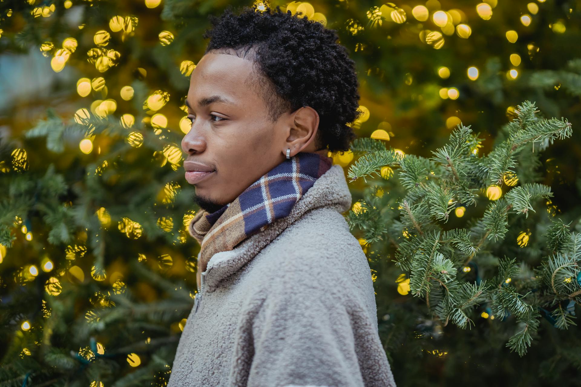 Side profile of a young man in festive winter attire with blurred holiday lights in the background.