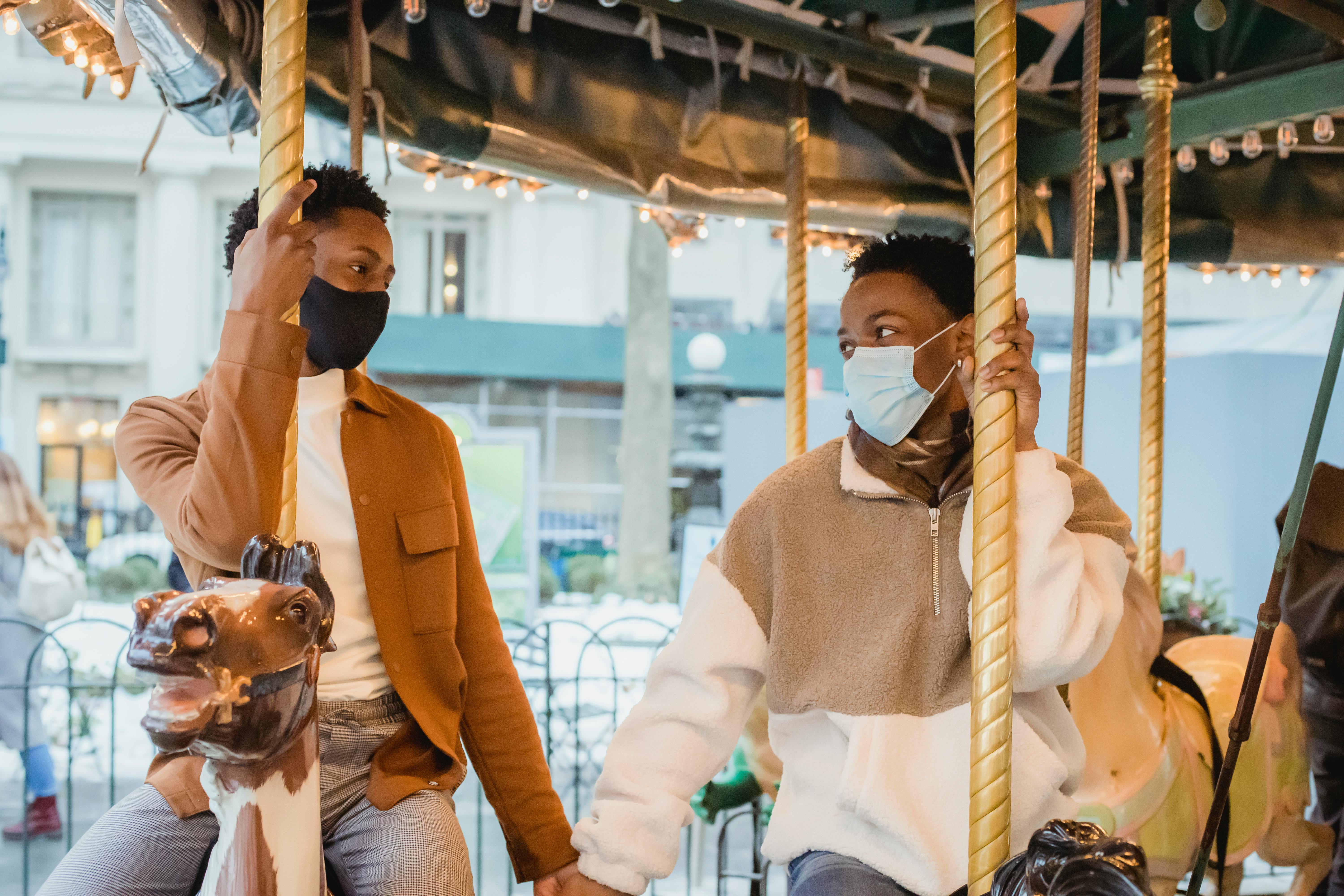 stylish loving african american gays holding hands while sitting on carousel