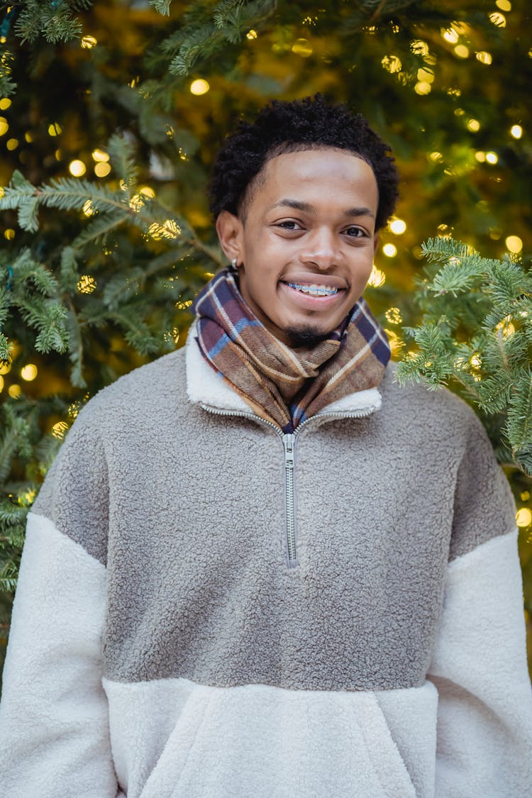 Content Young African American Guy Smiling At Camera Near Christmas Tree