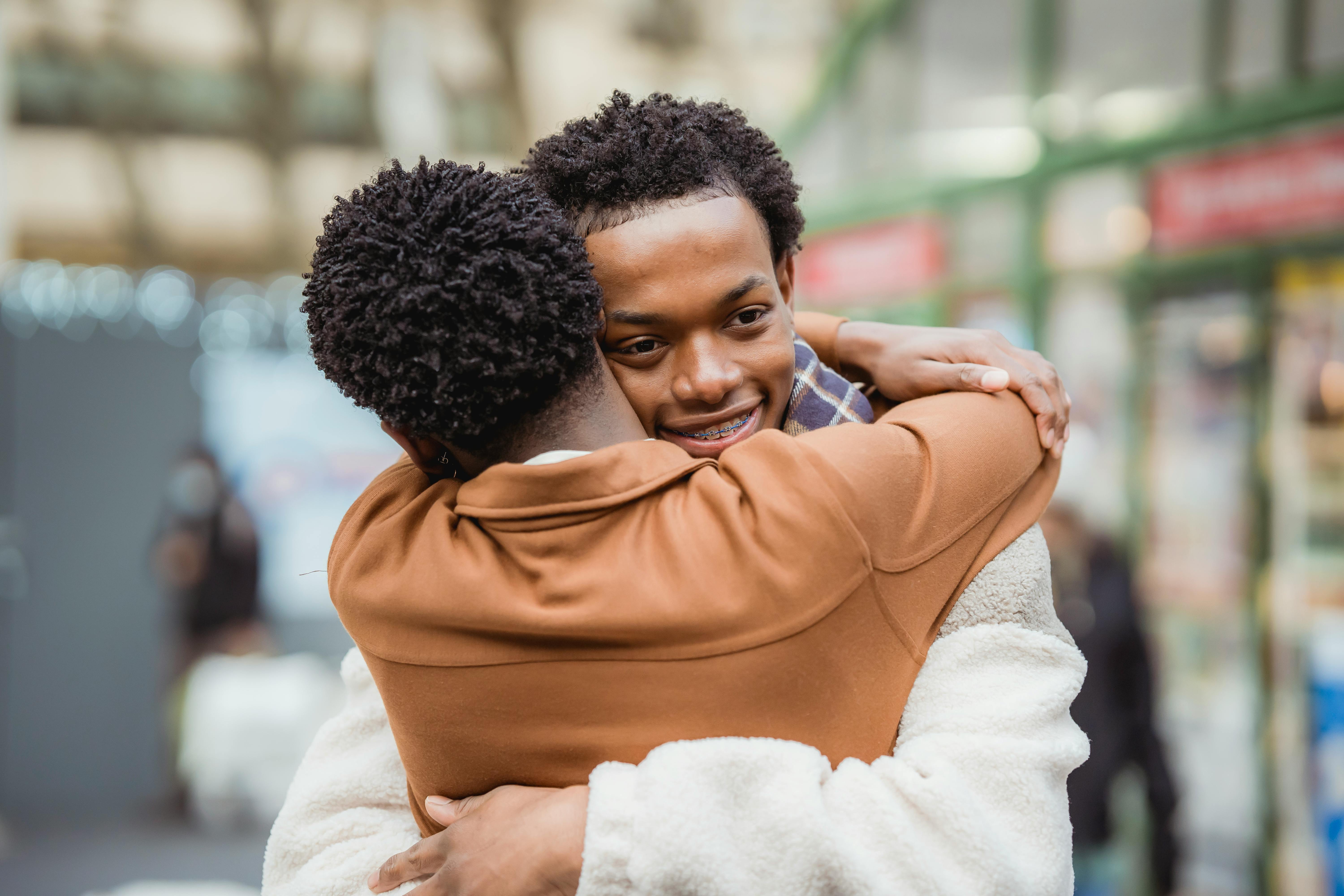 joyful young ethnic guys cuddling on street