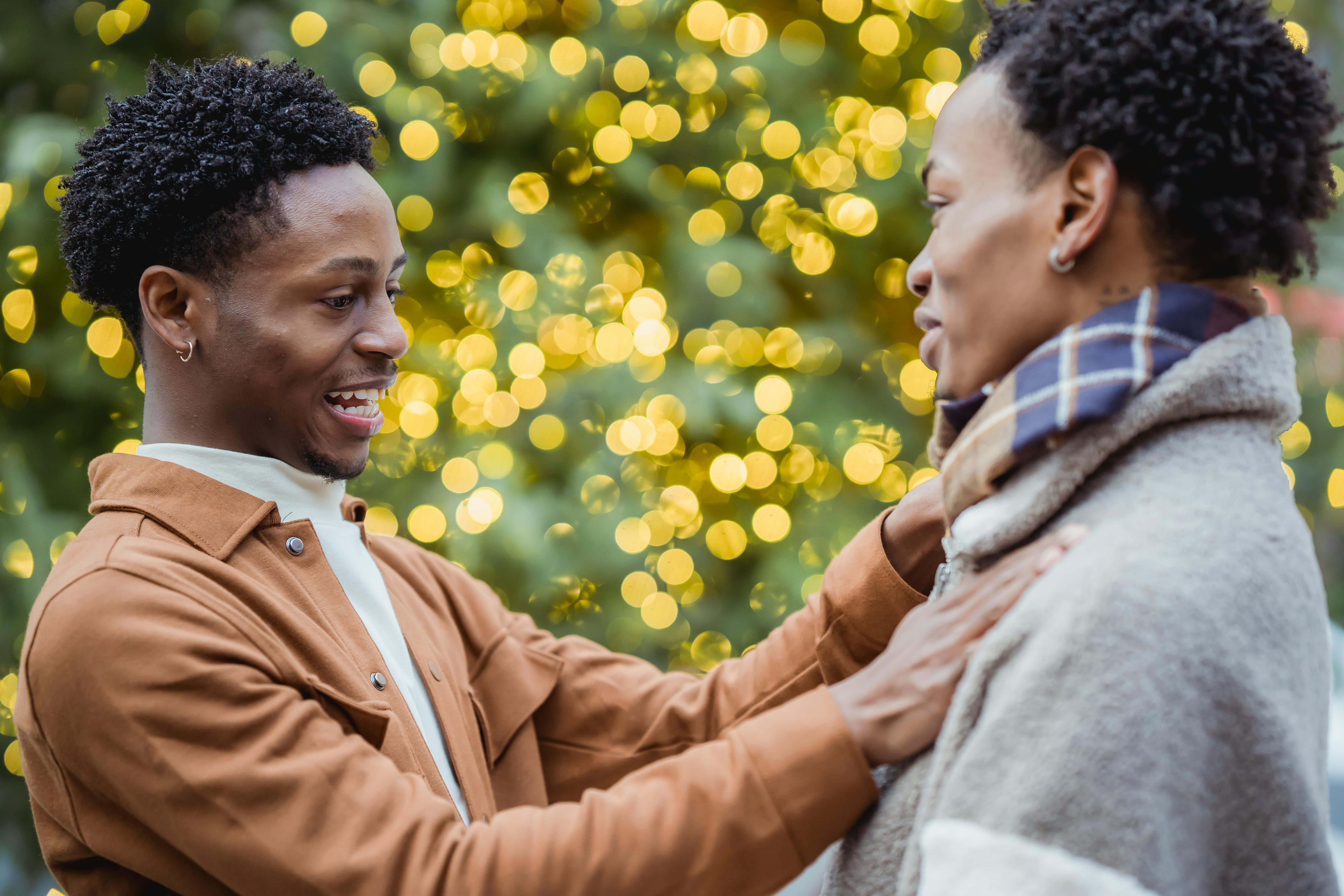 smiling young black man adjusting scarf of boyfriend on street