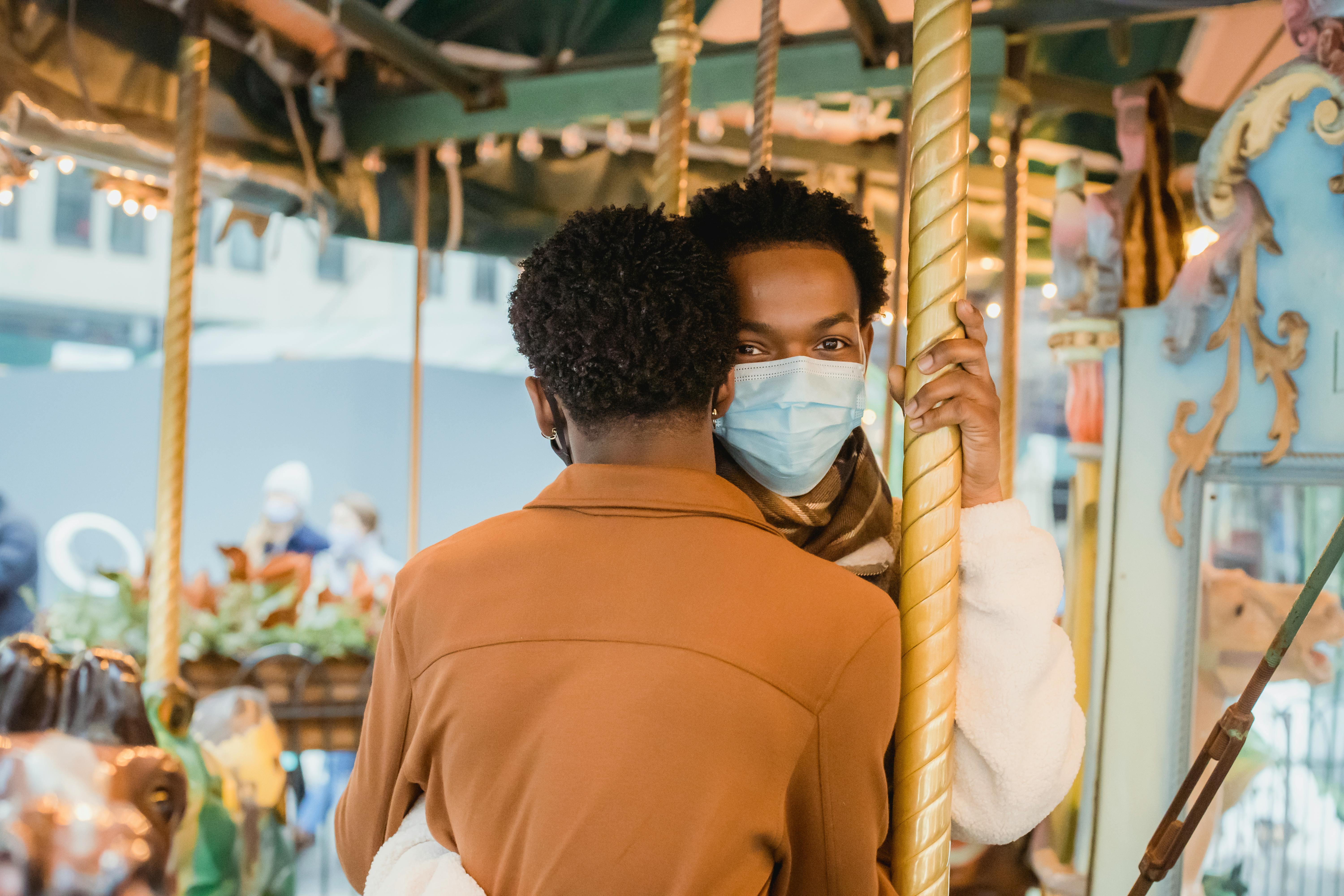 happy gay couple on carousel in medical masks