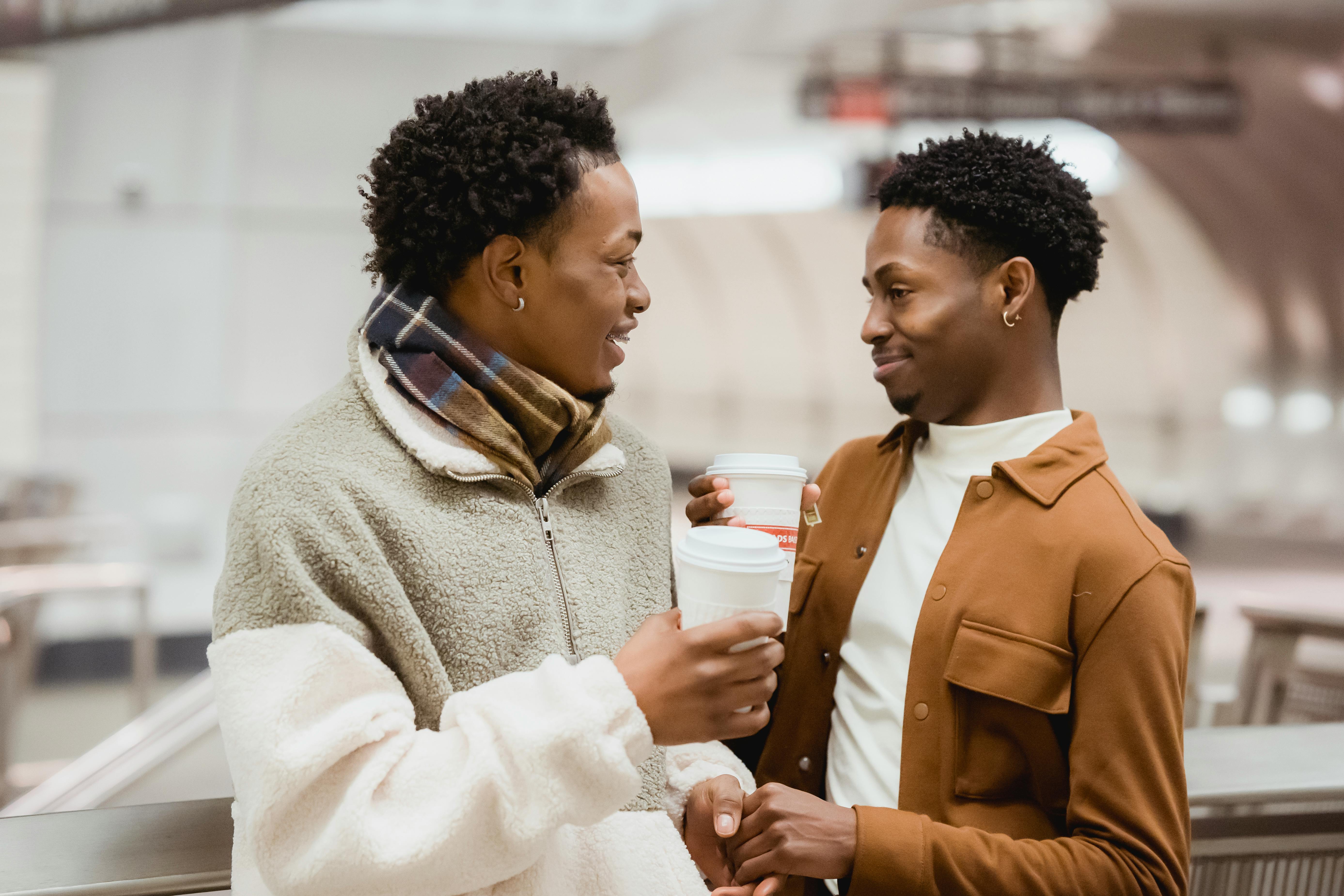 cheerful black homosexual couple with coffee talking in subway