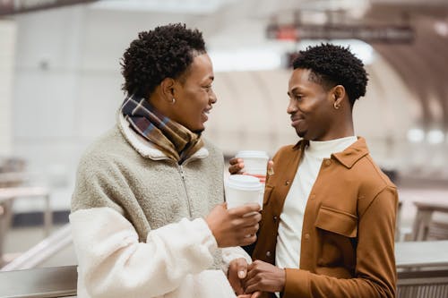 Free Cheerful black homosexual couple with coffee talking in subway Stock Photo