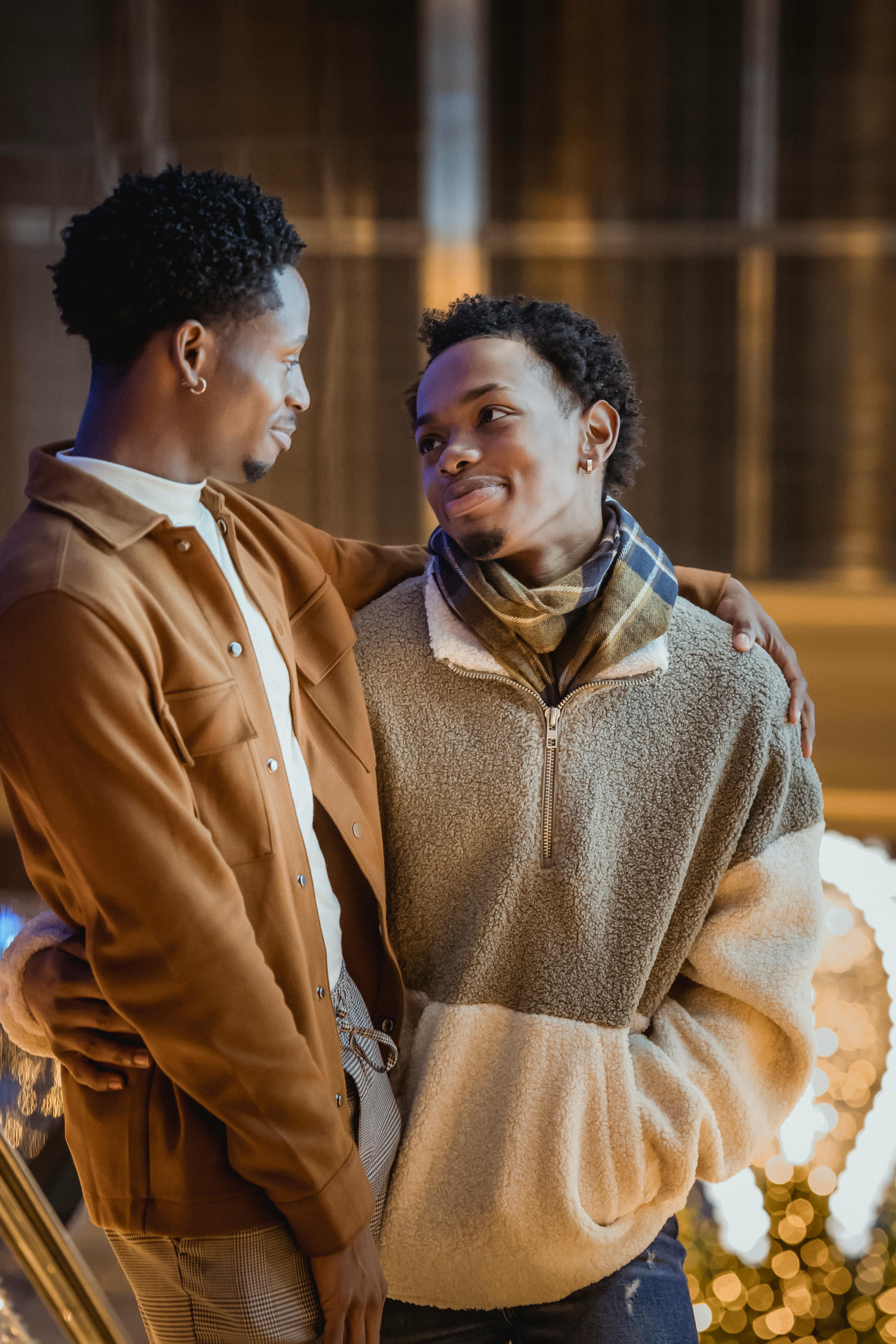 black gay couple hugging in street near decorations with garlands