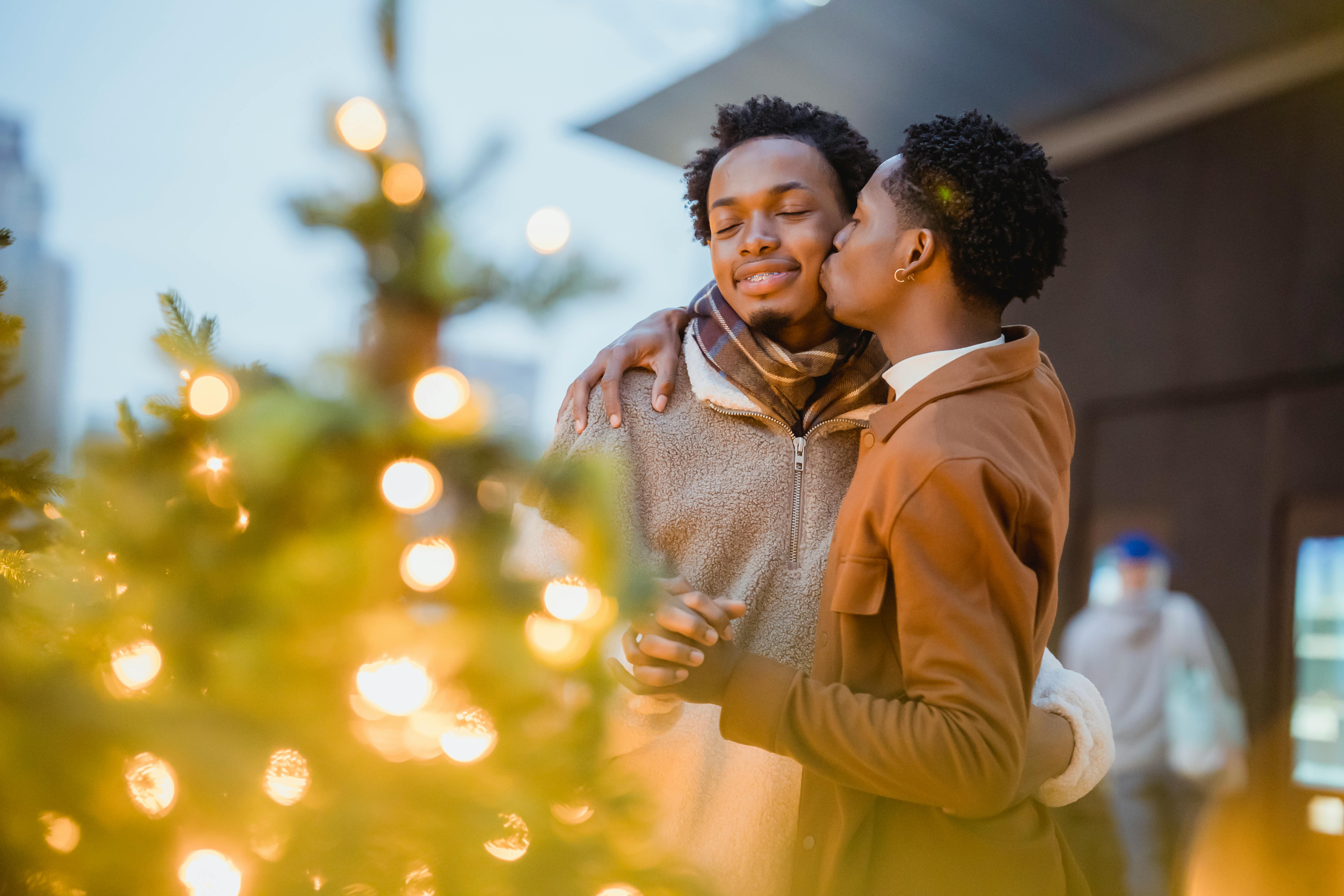 black gay couple embracing and kissing near decorated christmas trees