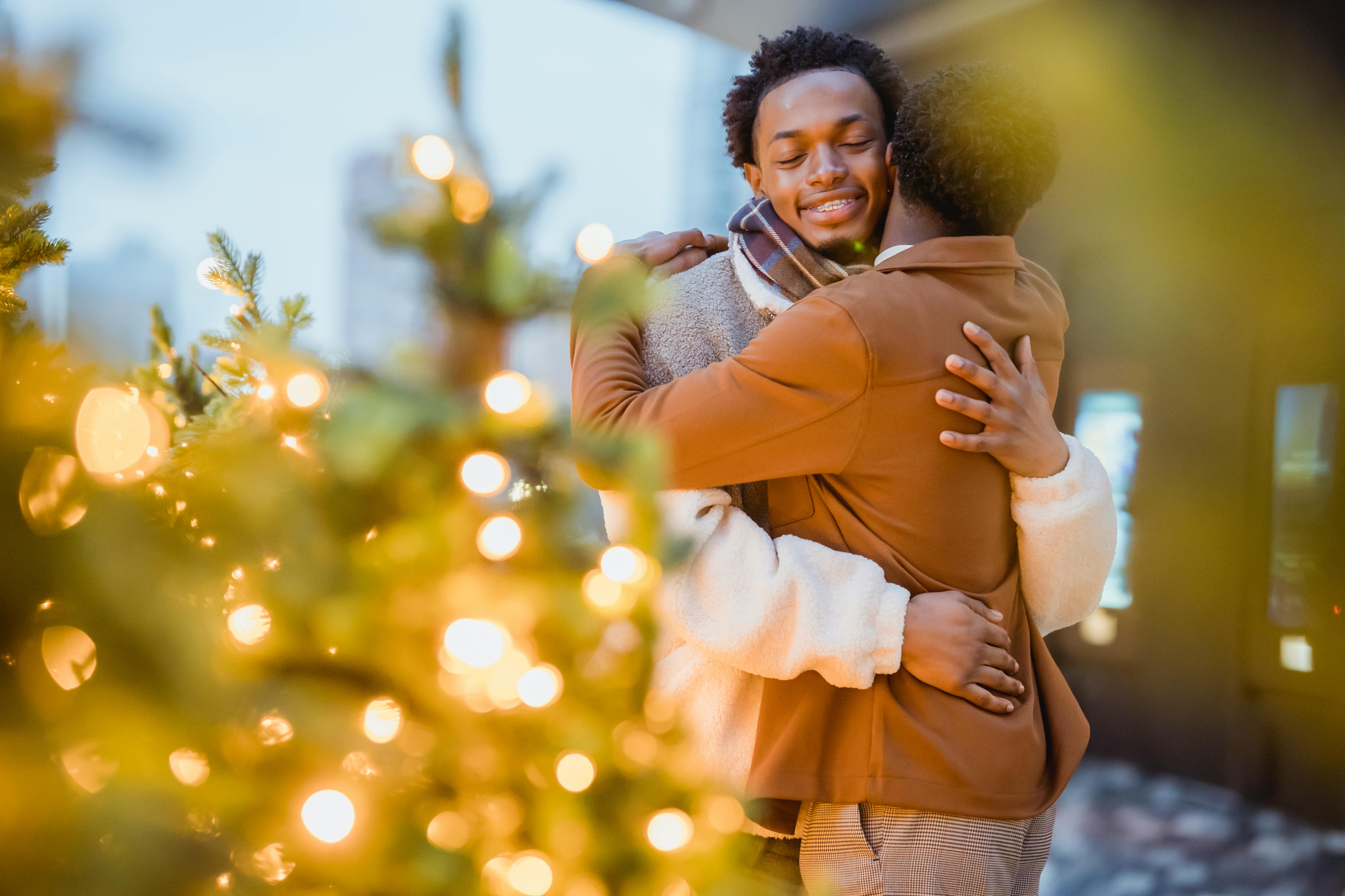 black gay couple hugging in street near decorated christmas trees