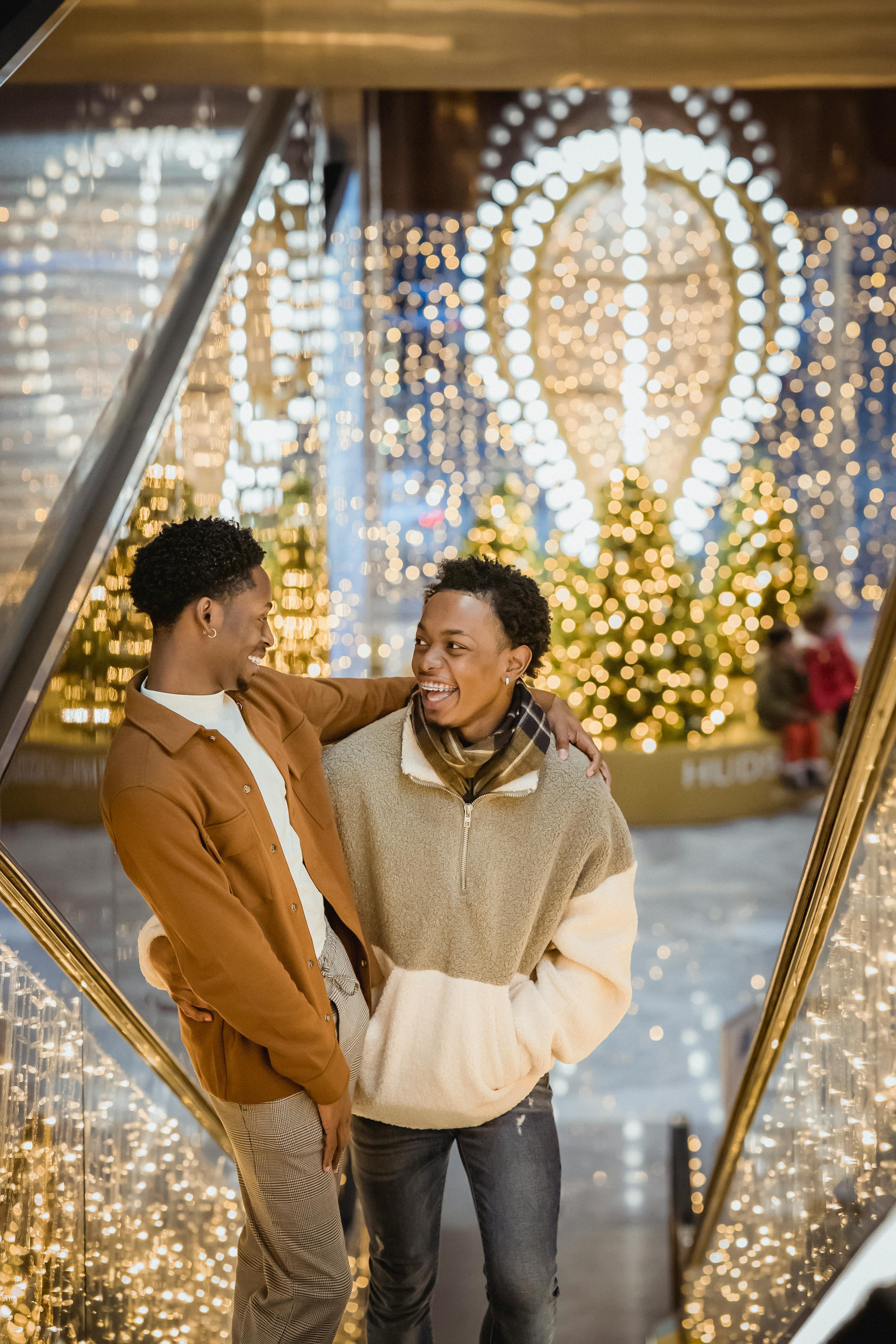 black gay couple on escalator in building near christmas decorations