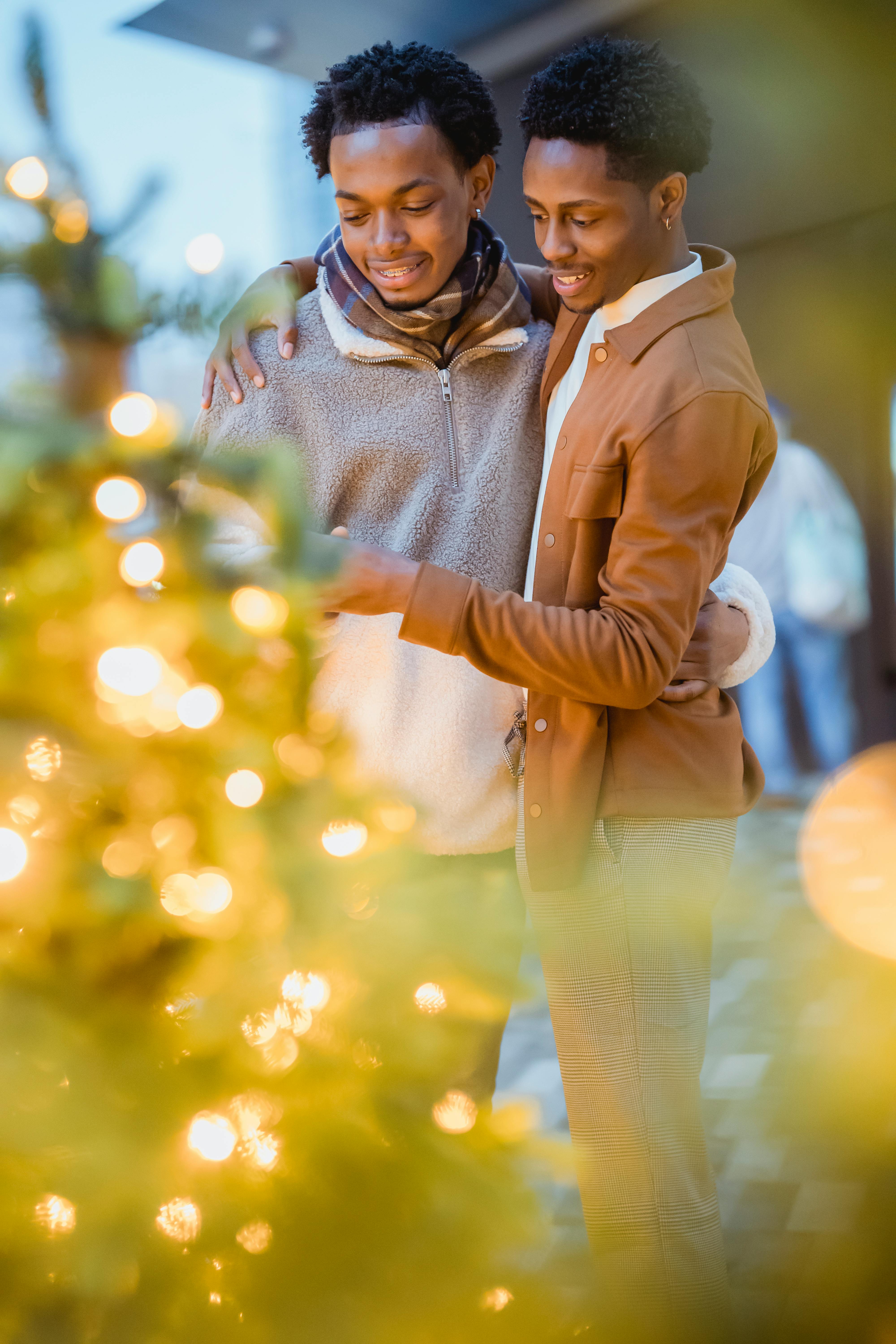 black gay couple embracing in street near decorated christmas trees