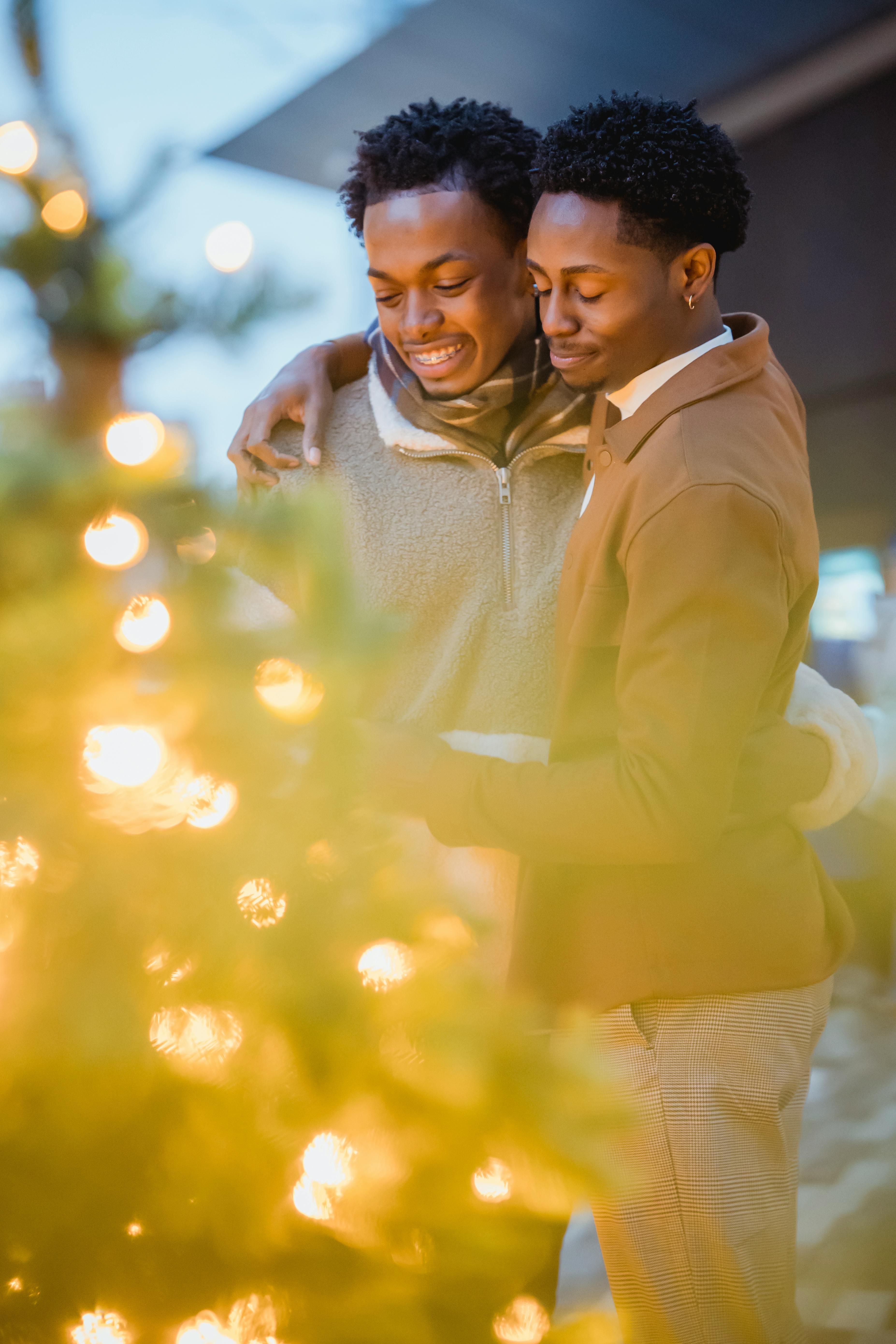 black gay couple embracing near decorated christmas trees in street