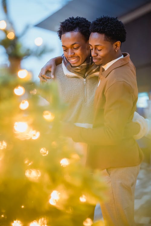 Black gay couple embracing near decorated Christmas trees in street