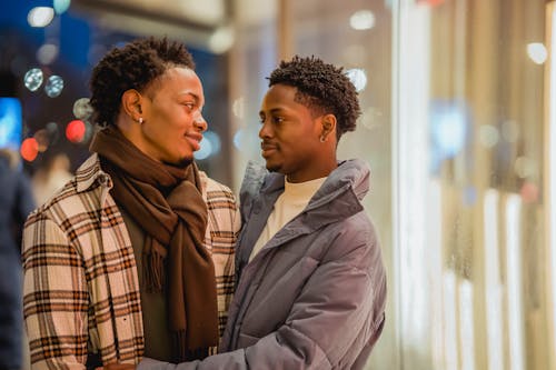 Free Romantic African American homosexual couple looking at each other while standing on street near building at evening time on blurred background Stock Photo