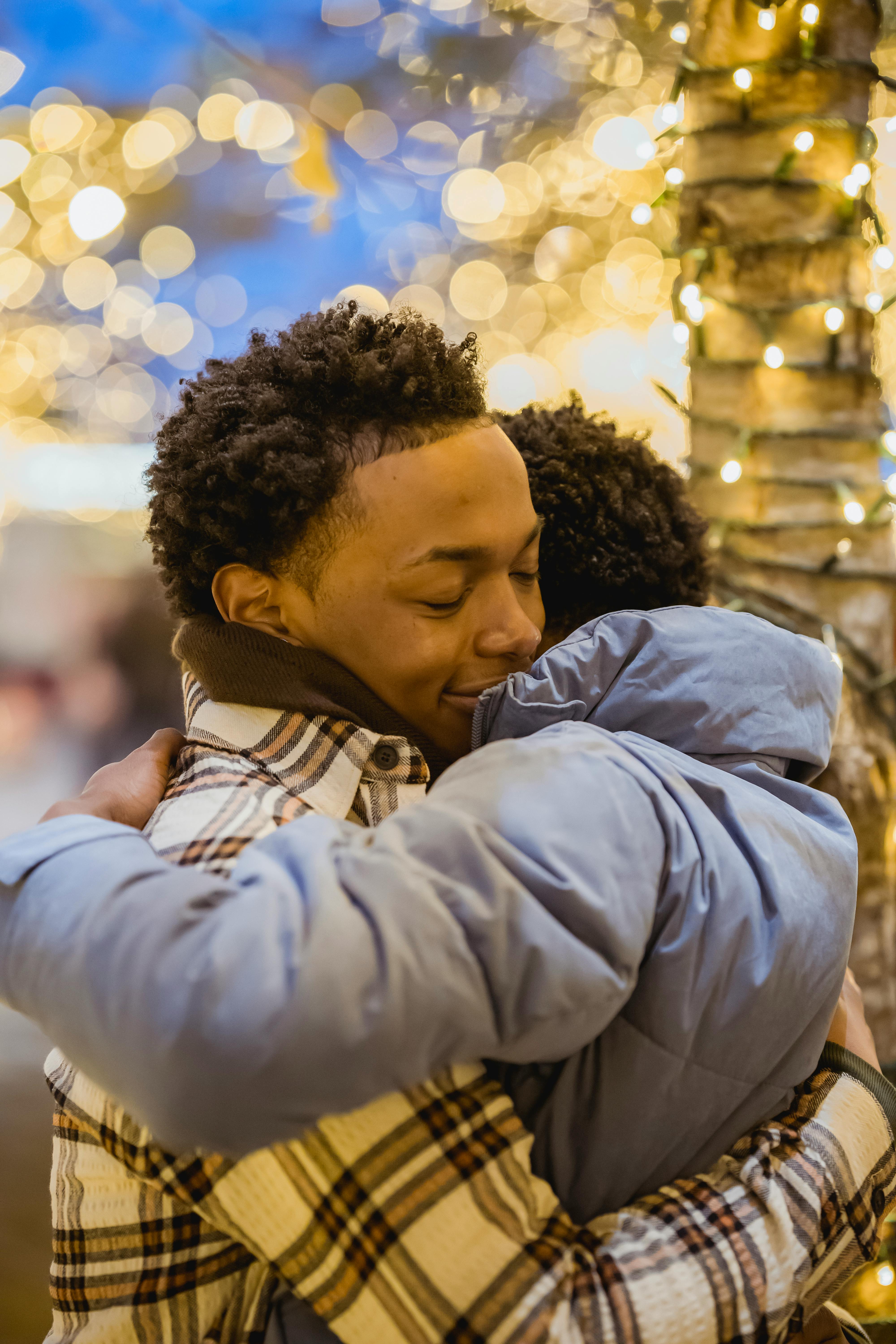 Two people embracing warmly under twinkling holiday lights, creating a festive and romantic atmosphere.