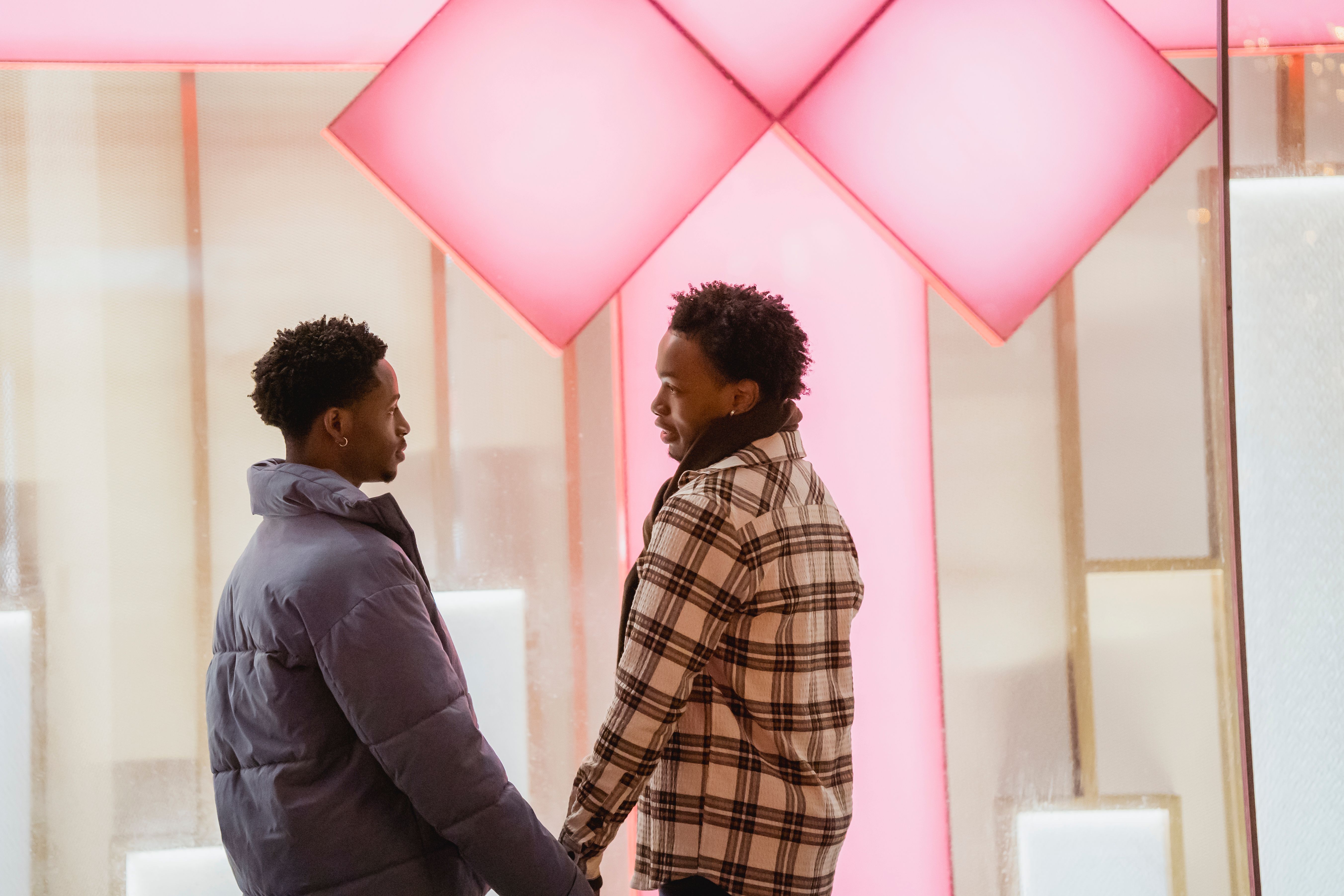 Side view of African American homosexual couple holding hands and looking at each other while standing near glass wall of house