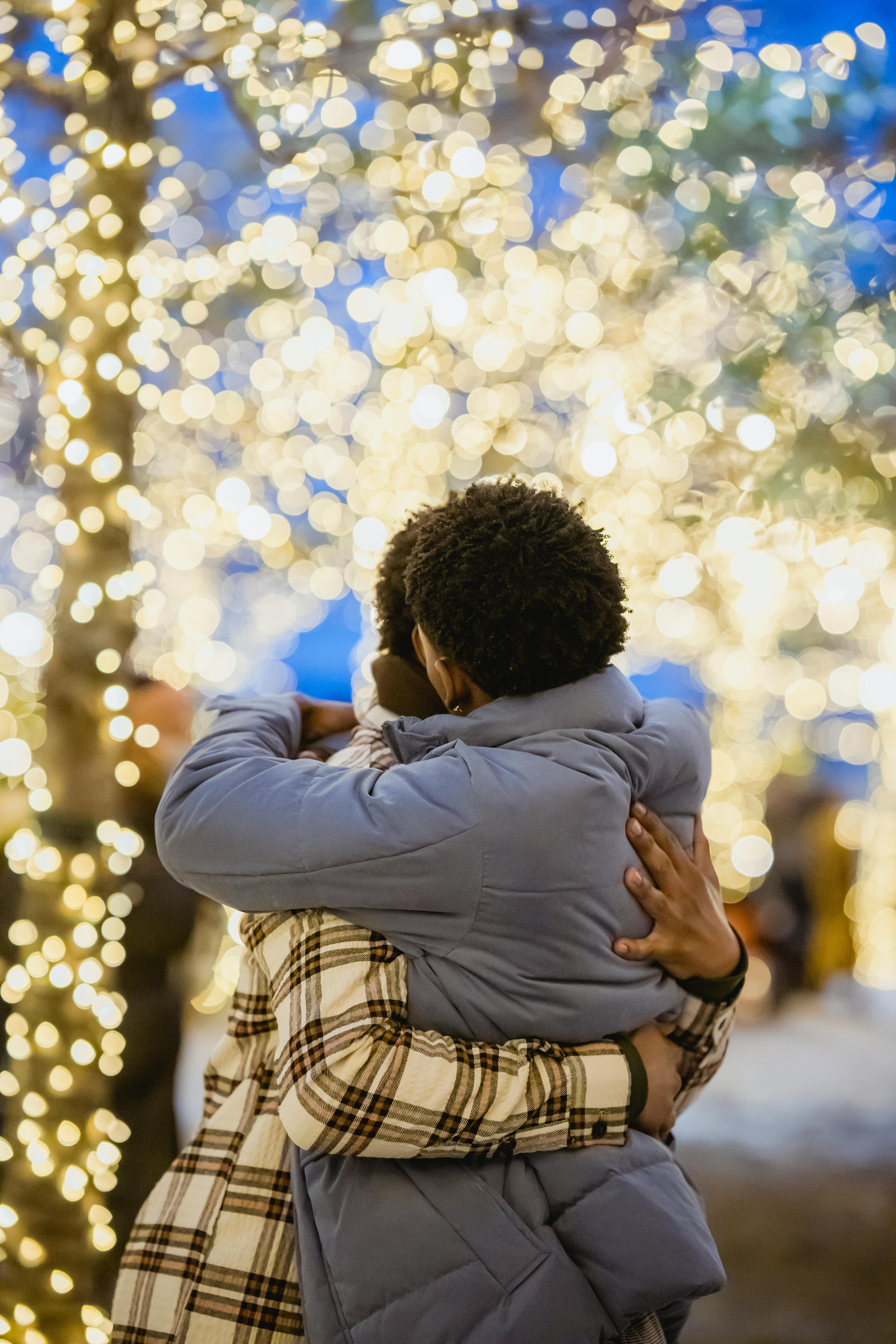 A loving couple embraces outdoors surrounded by glowing holiday lights, creating a romantic and festive atmosphere.