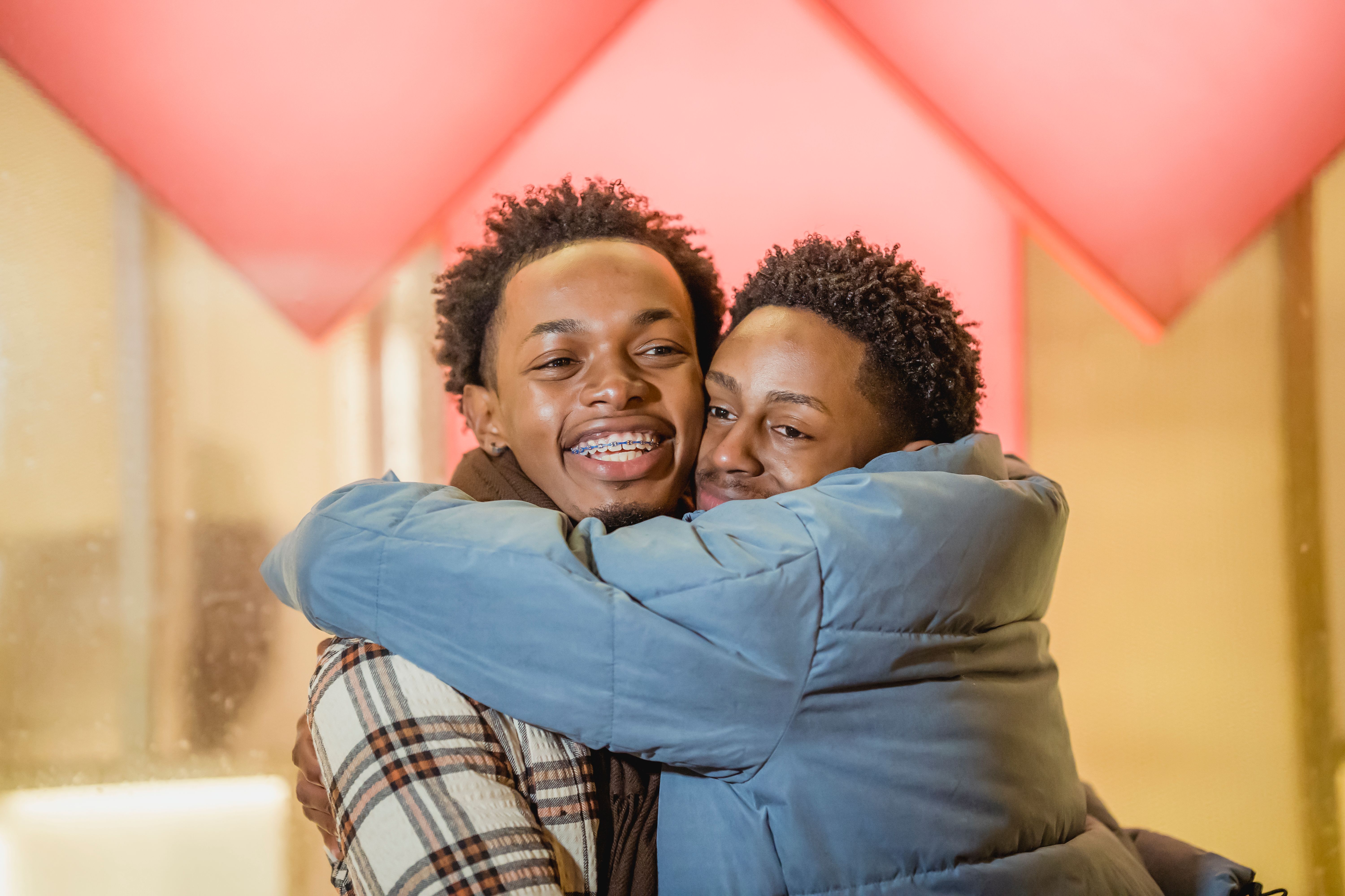 Two friends share a joyful hug outdoors against a vibrant background, symbolizing friendship and happiness.