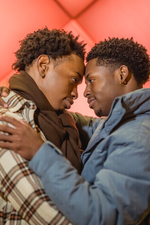 Side view of loving African American homosexual couple hugging and looking at each other while standing on street near building