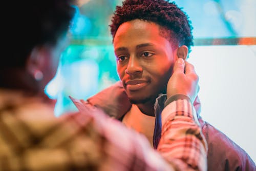 Crop anonymous African American male touching ears of smiling gentle boyfriend on glowing street