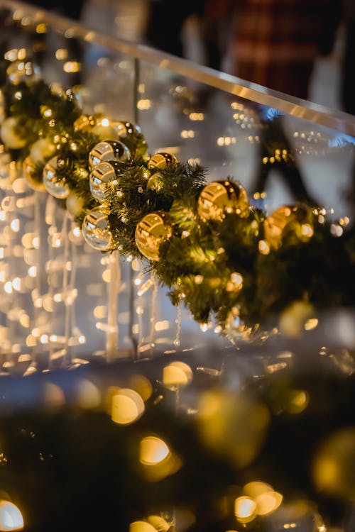 Green garland of spruce with glowing lights and baubles hanging on glass on blurred background