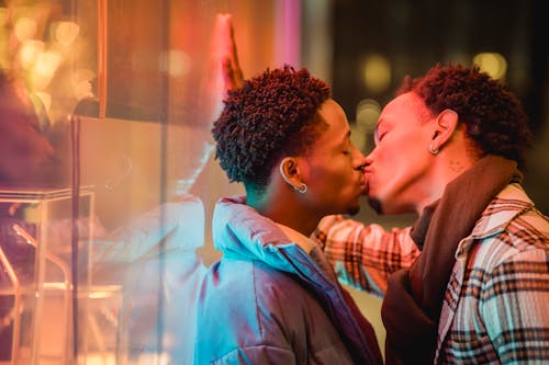 Black gays kissing on street near glass window