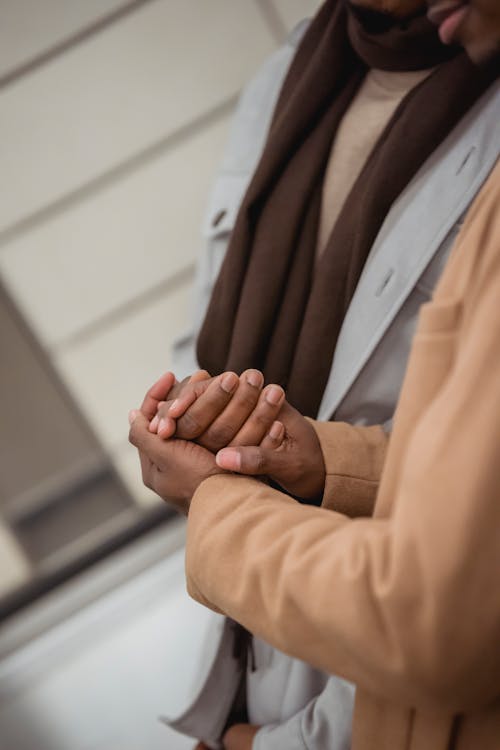 Crop unrecognizable African American couple in casual wear holding hands tenderly and standing on street