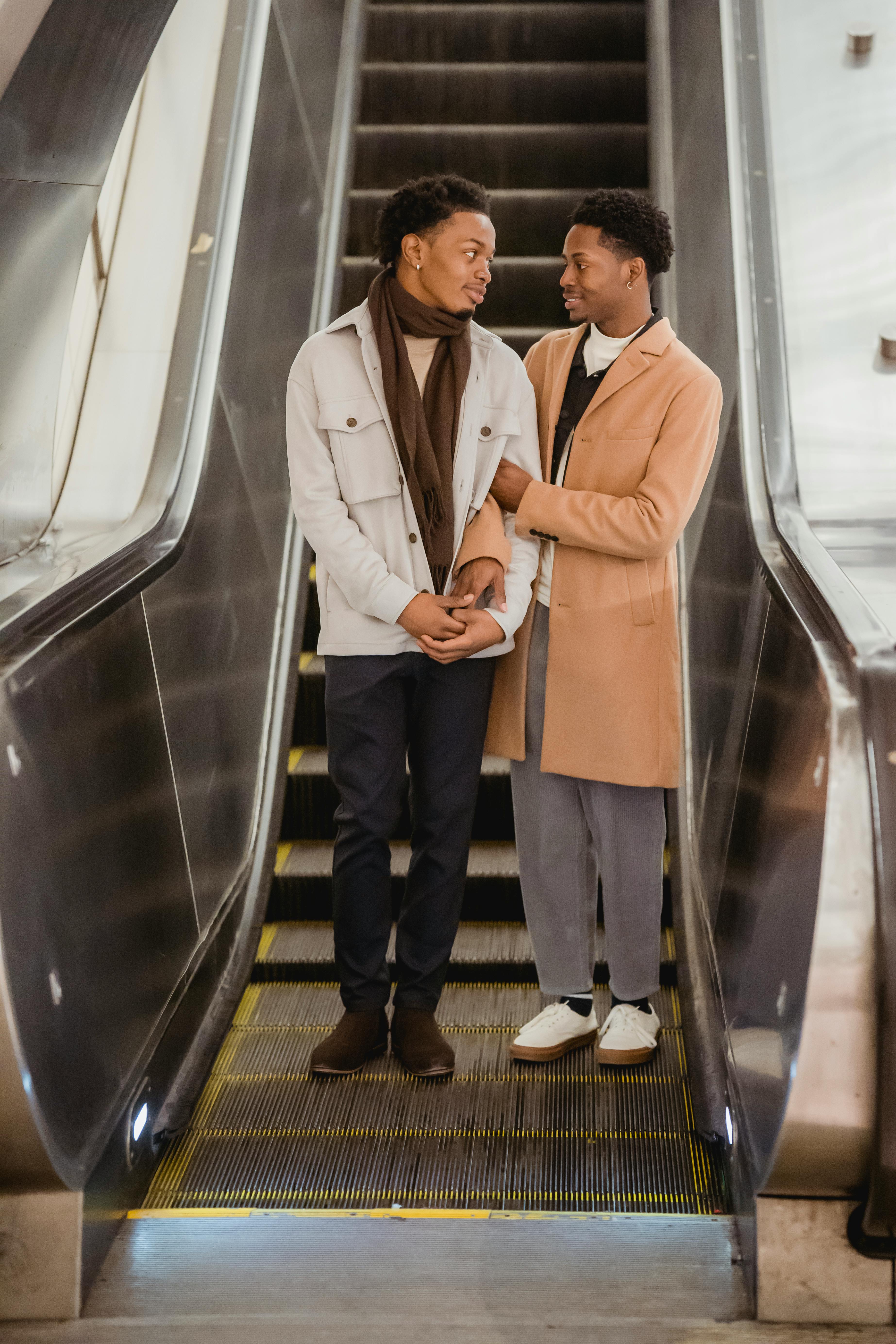 smiling black gay couple holding hands on escalator