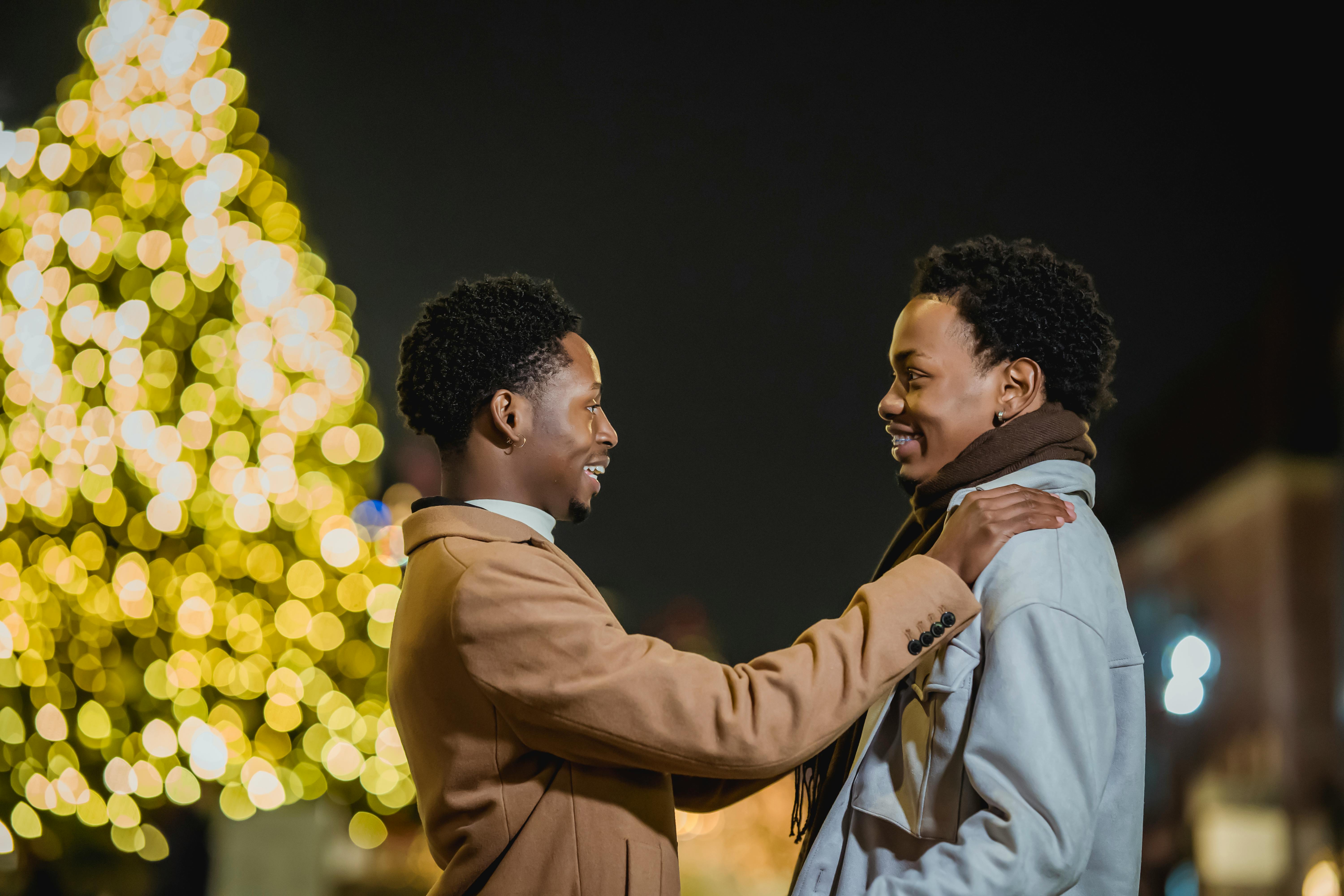 happy black couple standing against tree decorated with glowing garlands