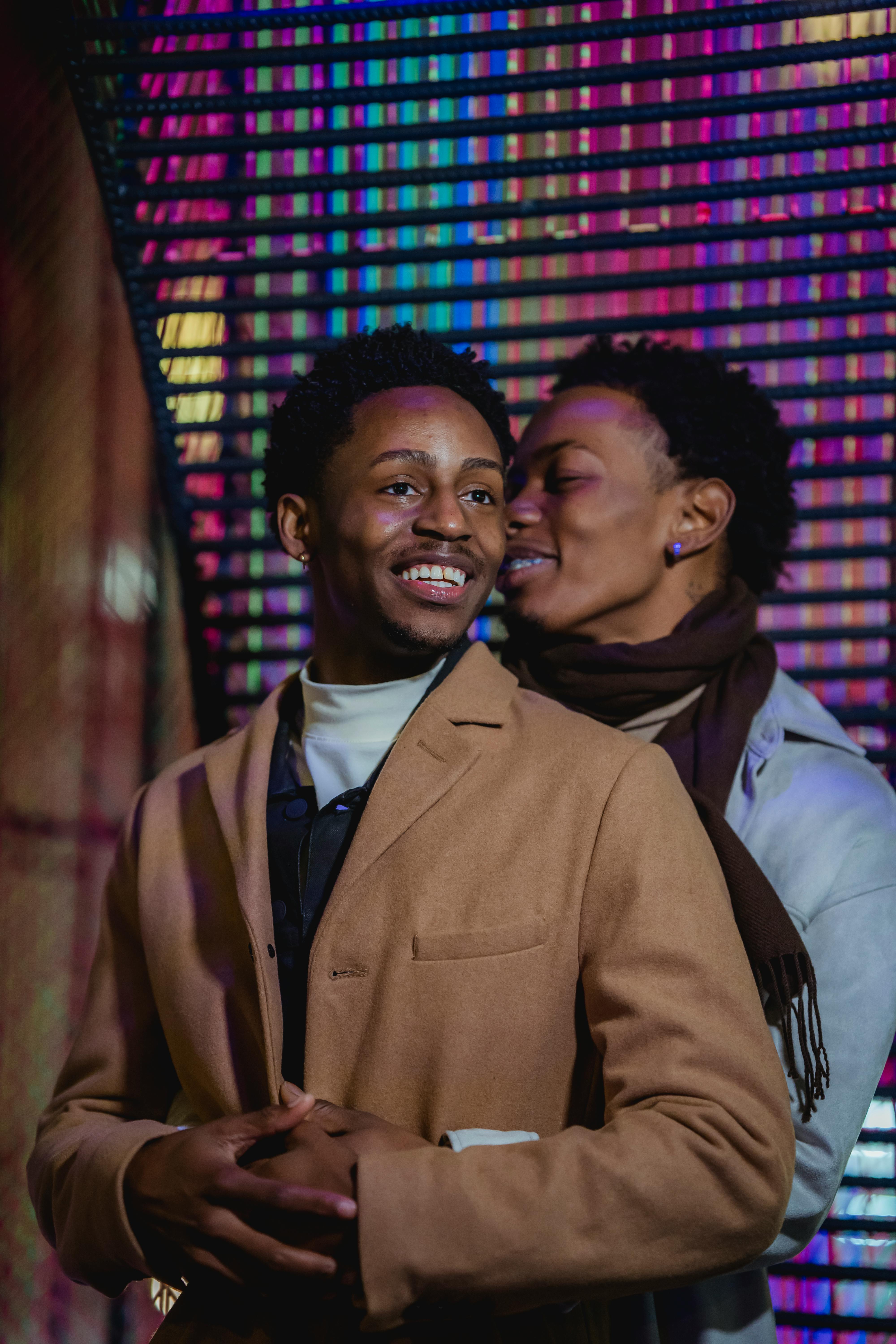 black couple caressing and hugging against wall with bright lights