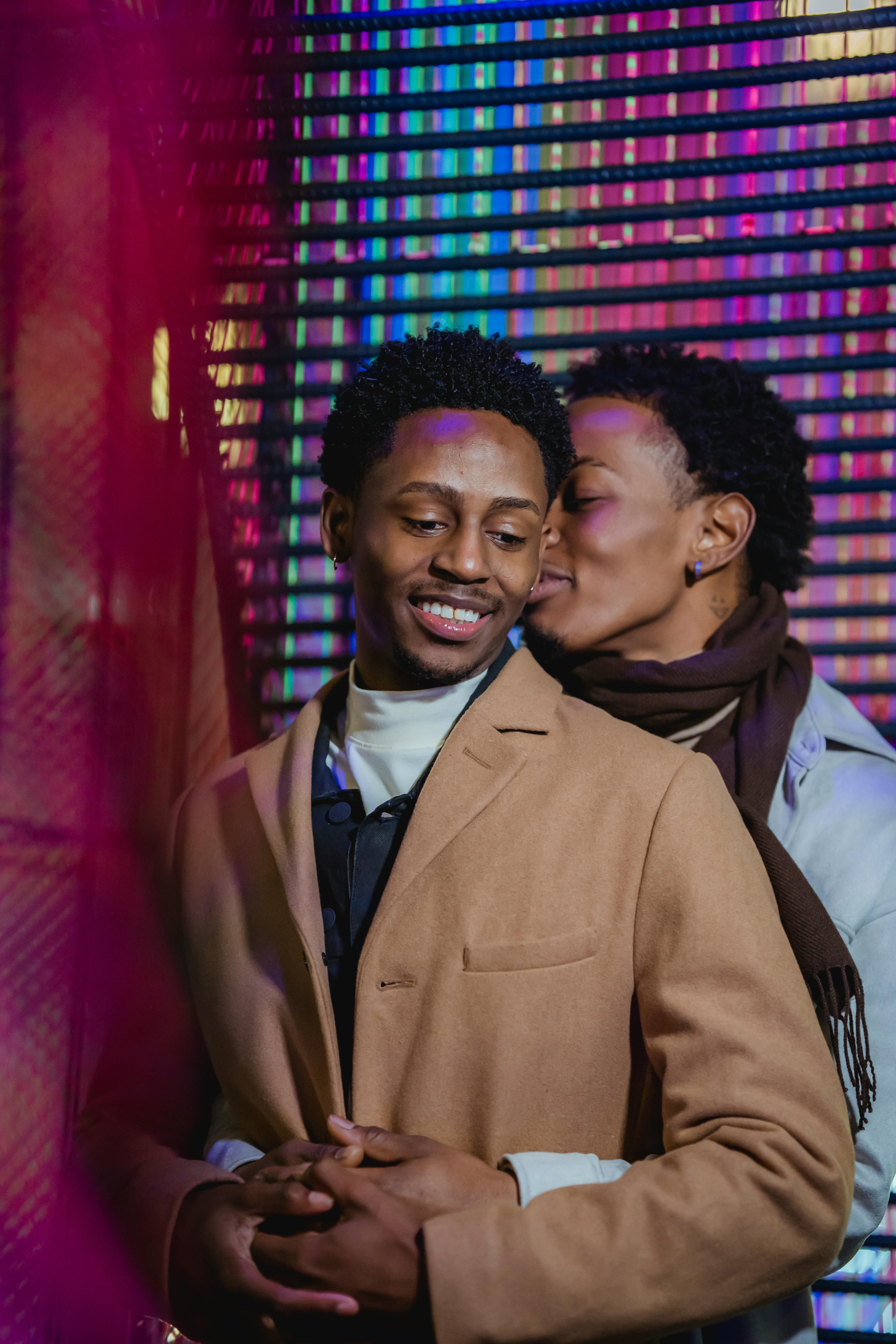 positive black same sex couple embracing gently against colorful wall