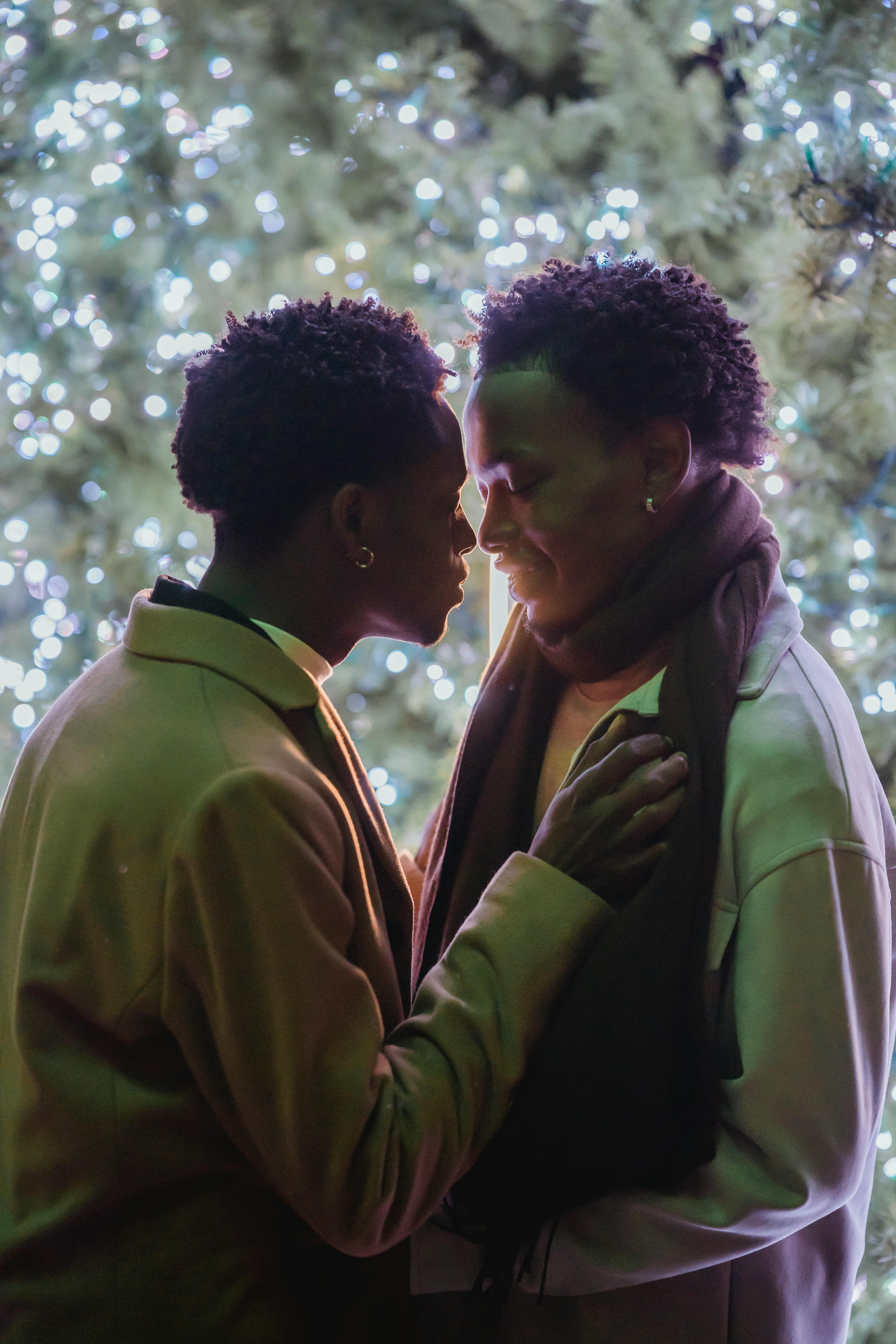 loving black same sex couple embracing against evergreen tree