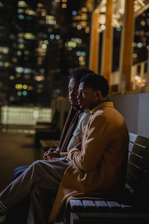 Black male partners sitting on bench in park