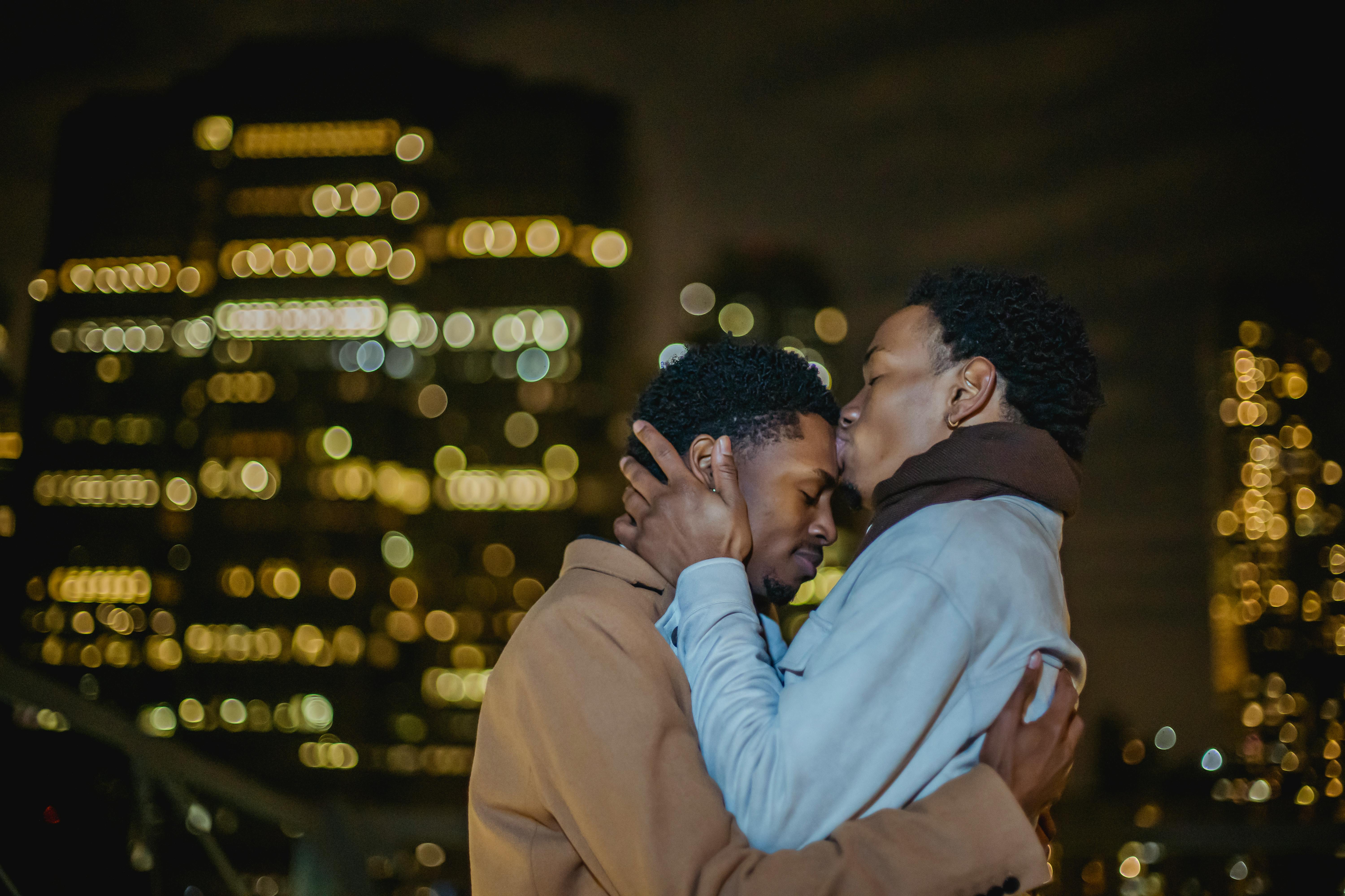 black homosexual male couple kissing while cuddling in city street