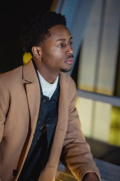 Free Side view of African American male in elegant clothes standing near railing of metal construction in city in evening time Stock Photo
