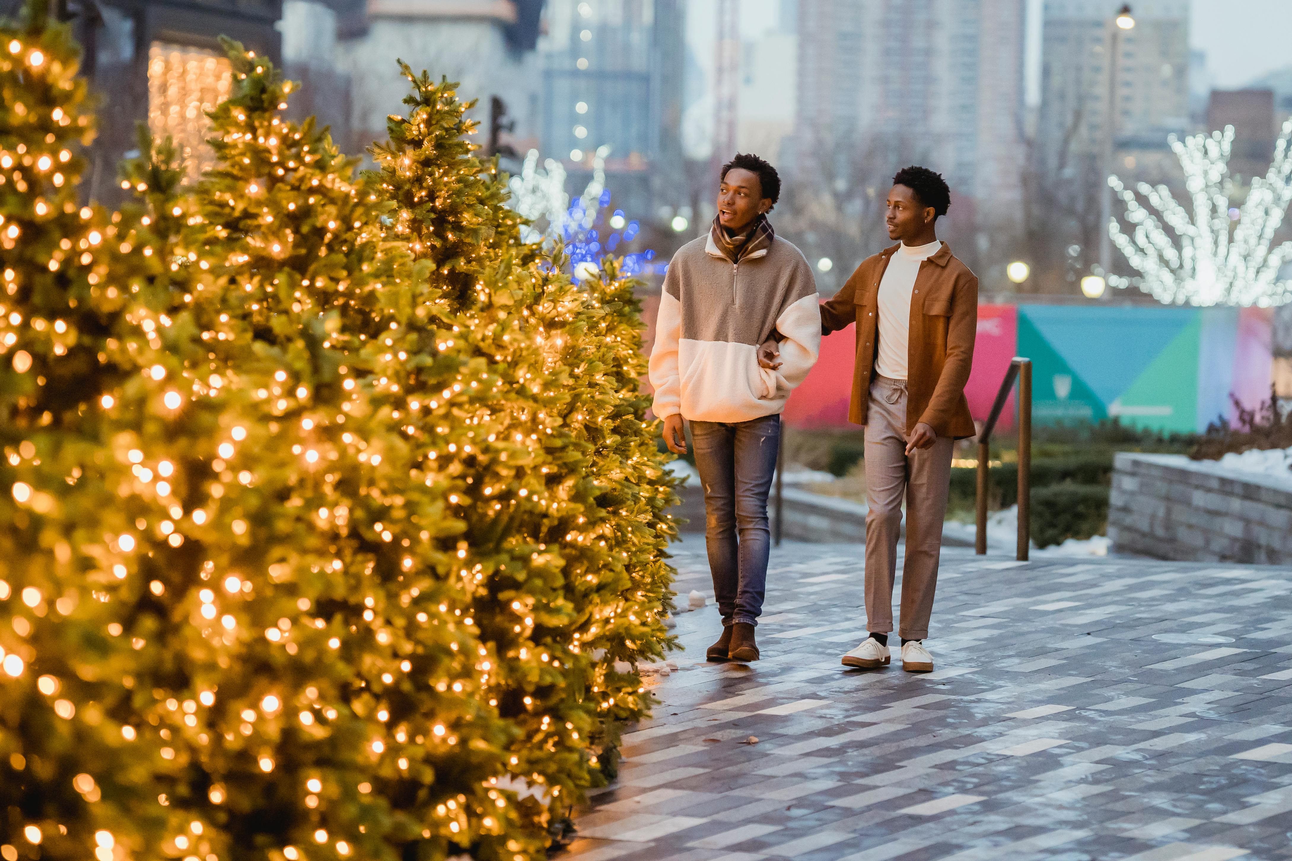 homosexual black couple walking on city pavement with christmas trees