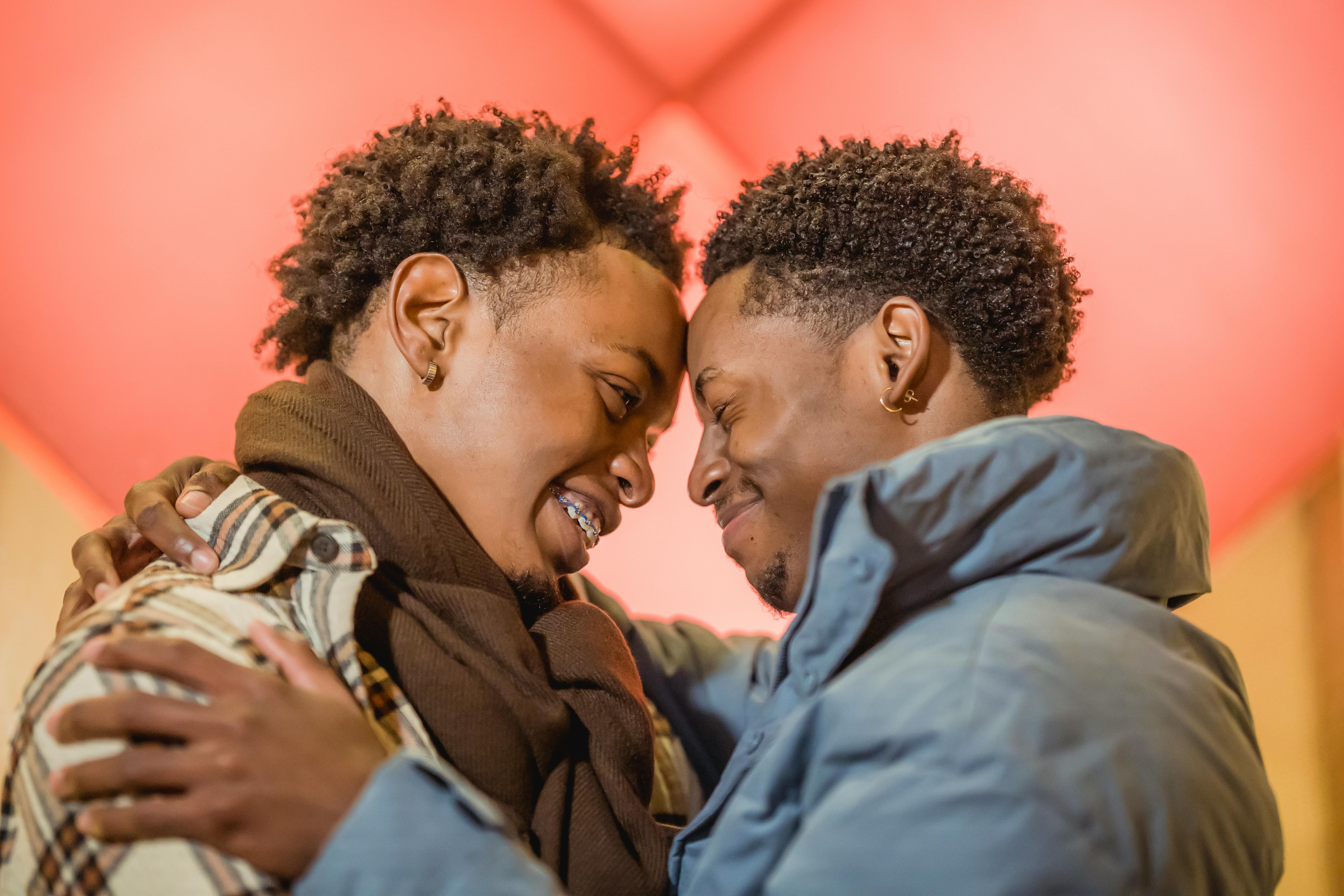 smiling homosexual black couple in outerwear embracing on colorful background