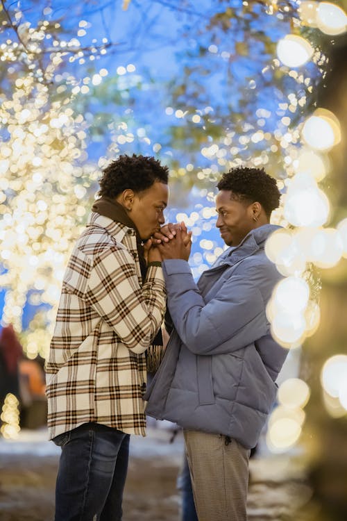 Side view of young black man kissing hand of boyfriend while looking at each other in town with shiny lights