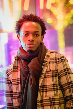 Young ethnic male in checkered jacket and scarf looking at camera in twilight on blurred background