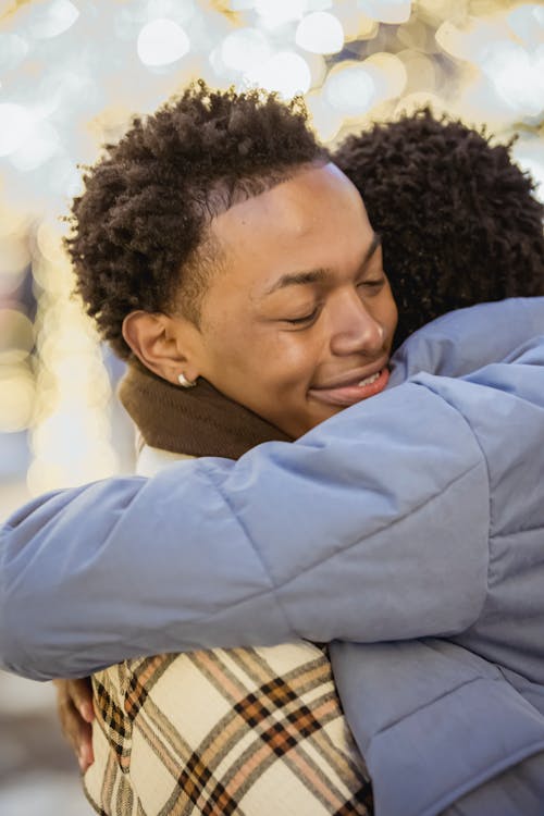 Smiling black man embracing unrecognizable boyfriend in outerwear