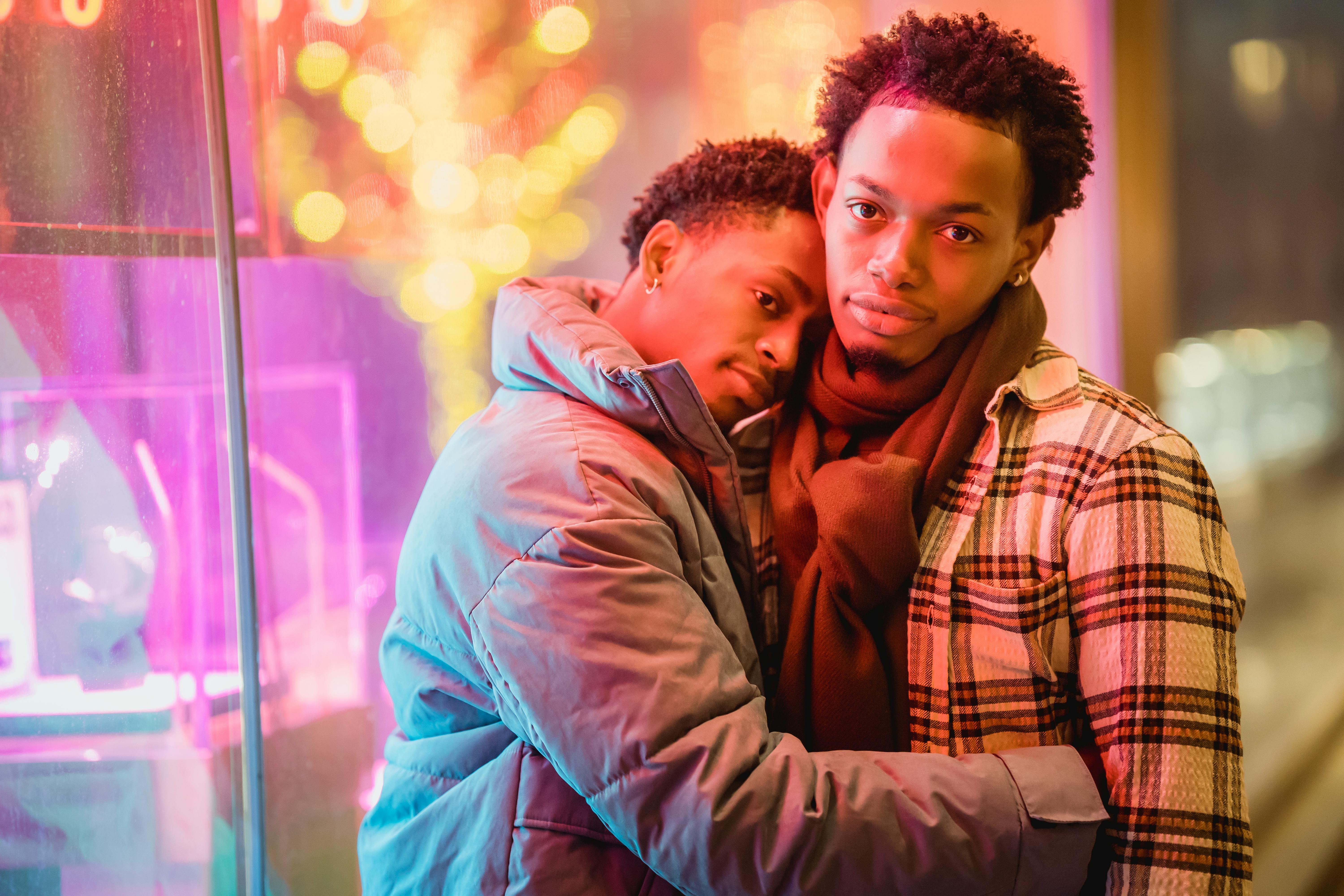 beloved young ethnic guys hugging on city street at night