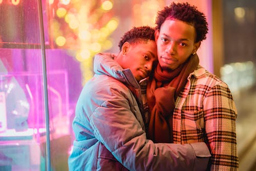 Beloved young ethnic guys hugging on city street at night