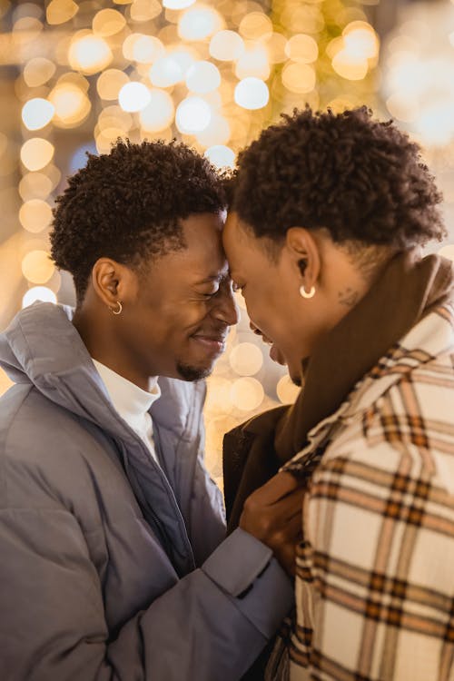 Smiling ethnic gay couple touching foreheads on street at night