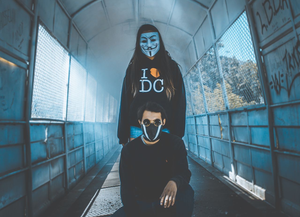 two masked individuals pose in a graffiti covered urban tunnel evoking