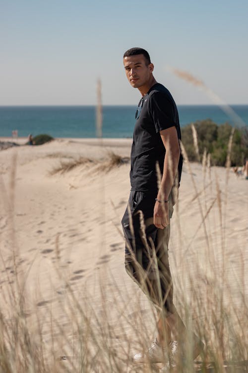 Gratis Pria Berkaus Hitam Dan Celana Coklat Berdiri Di Pantai Foto Stok