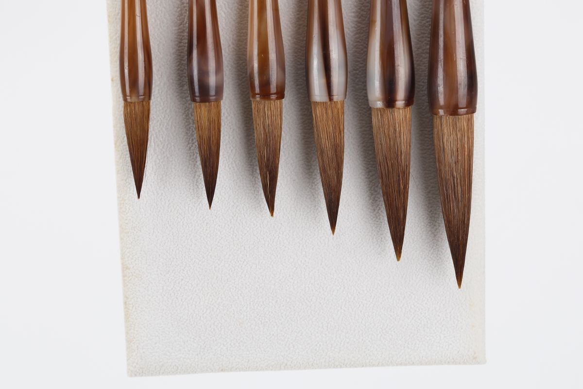 Six calligraphy brushes laid out on paper