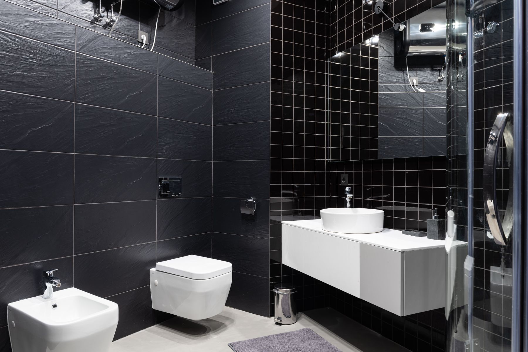 Bathroom with black tiled walls, sink, mirror and contemporary fixtures
