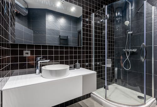 Interior of stylish modern bathroom with ceramic sink and shower unit with transparent glass doors and mirror