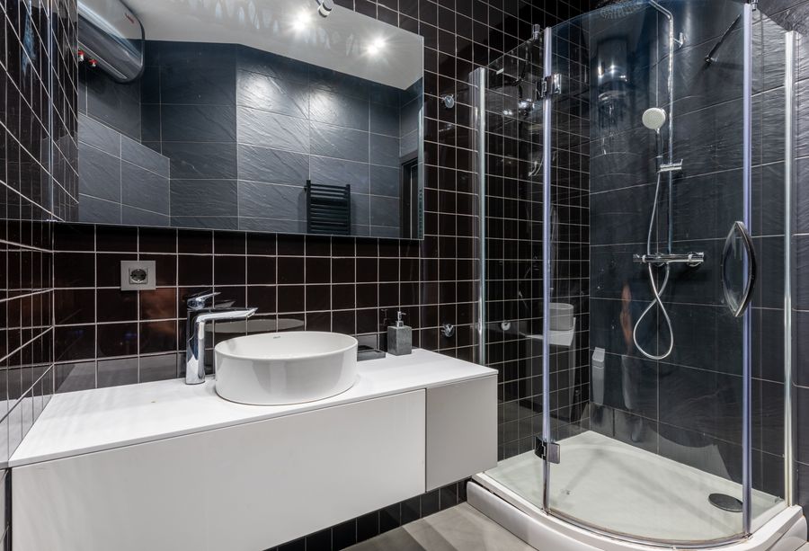 Dark-tiled bathroom with a glass shower cubicle and wall-hung basin